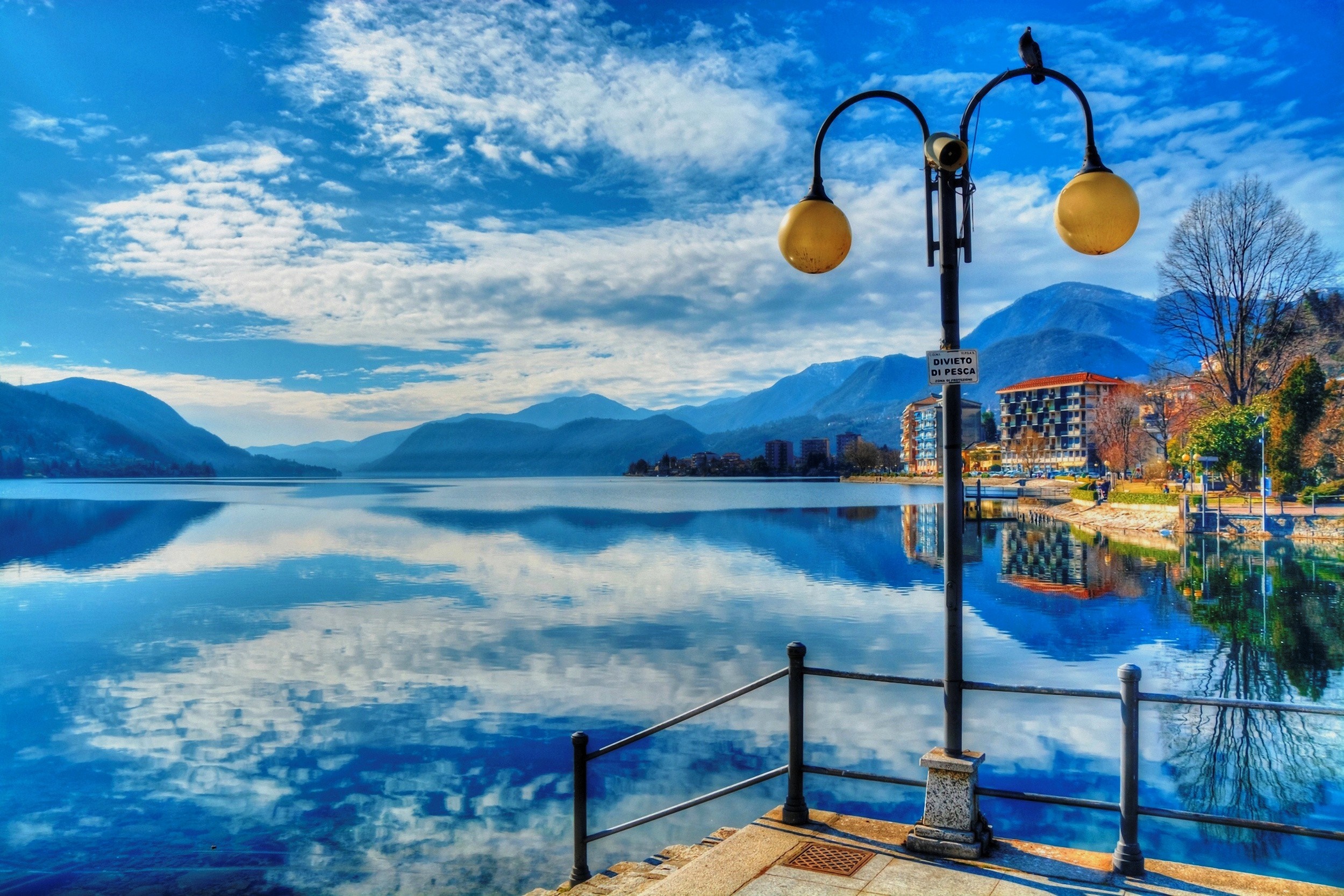 Lake with mountains and buildings under a blue sky HD Wallpaper