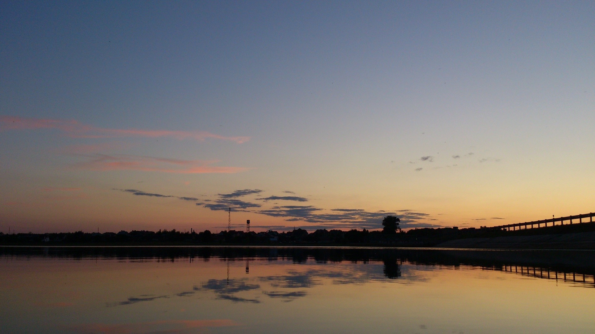 Sunset over a calm body of water with a silhouetted town HD Wallpaper