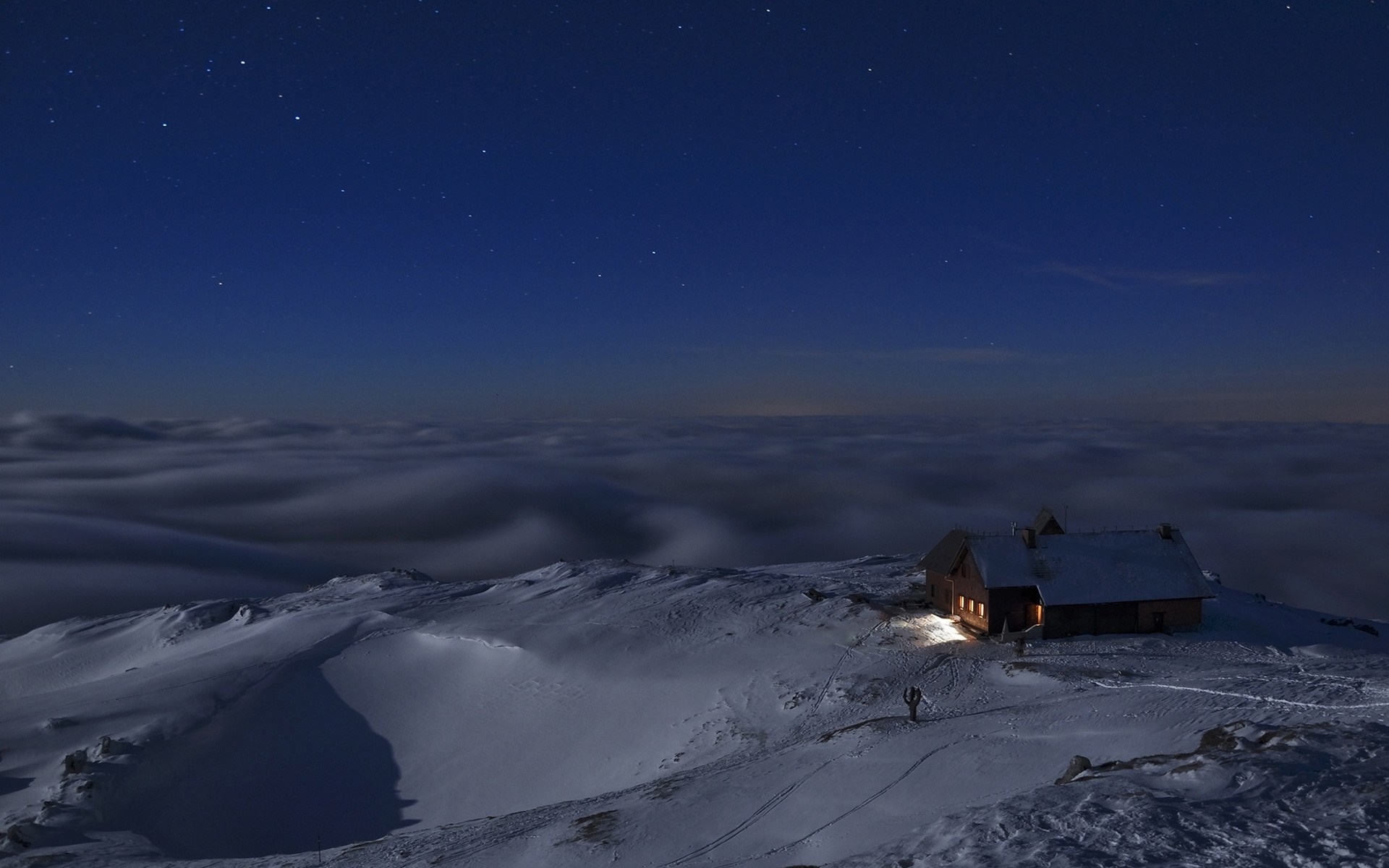 Snowy mountain hut under a starry night sky with clouds HD Wallpaper