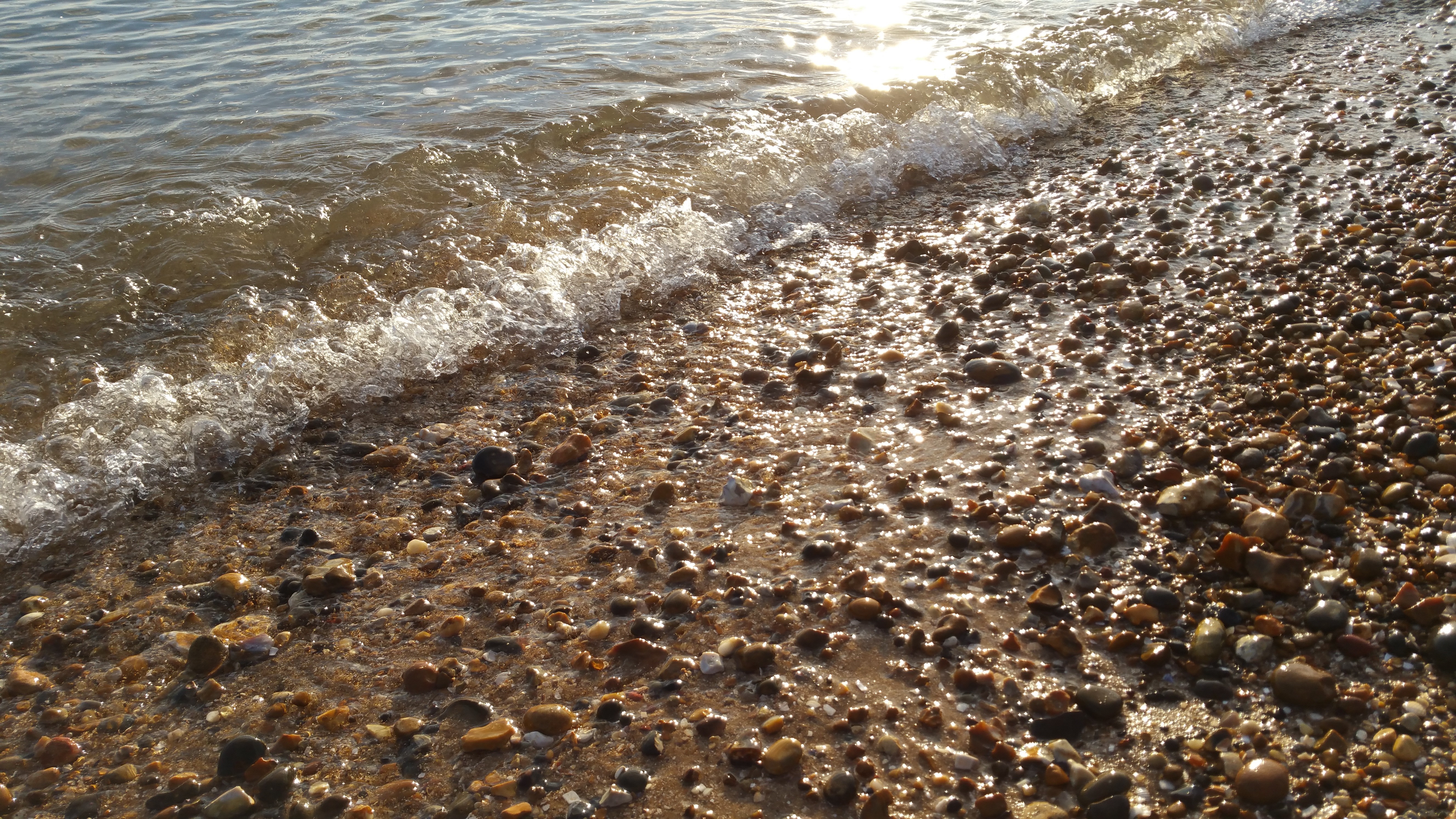 Sunlight on a pebble beach with gentle waves HD Wallpaper