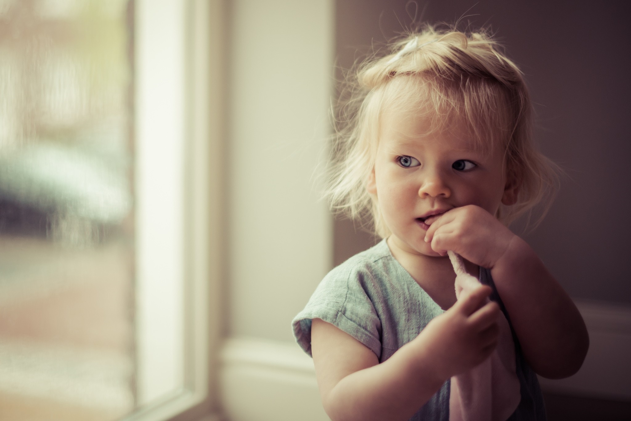 A toddler with blonde hair looking out a window HD Wallpaper