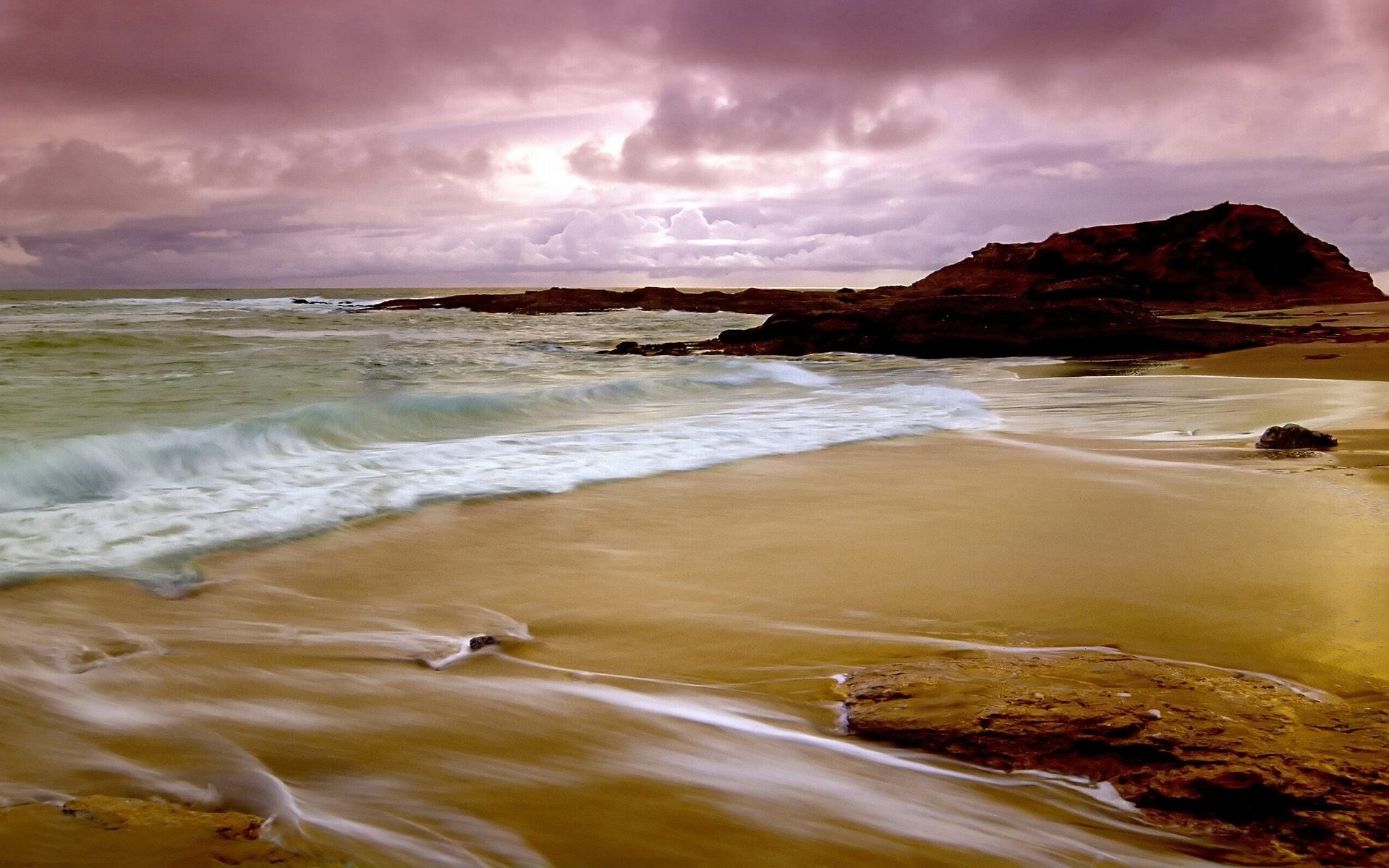 Ocean waves crashing on a sandy beach with rocky outcrops HD Wallpaper