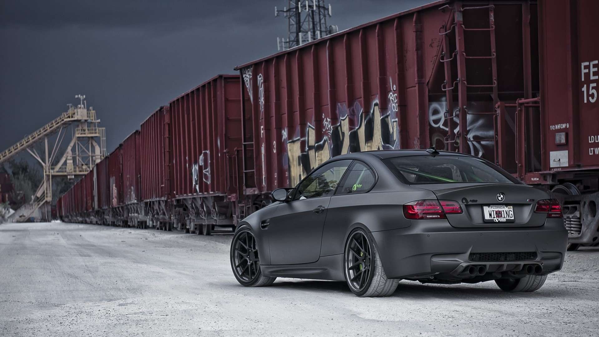 Matte black BMW M3 coupe parked by graffiti-covered train cars HD Wallpaper