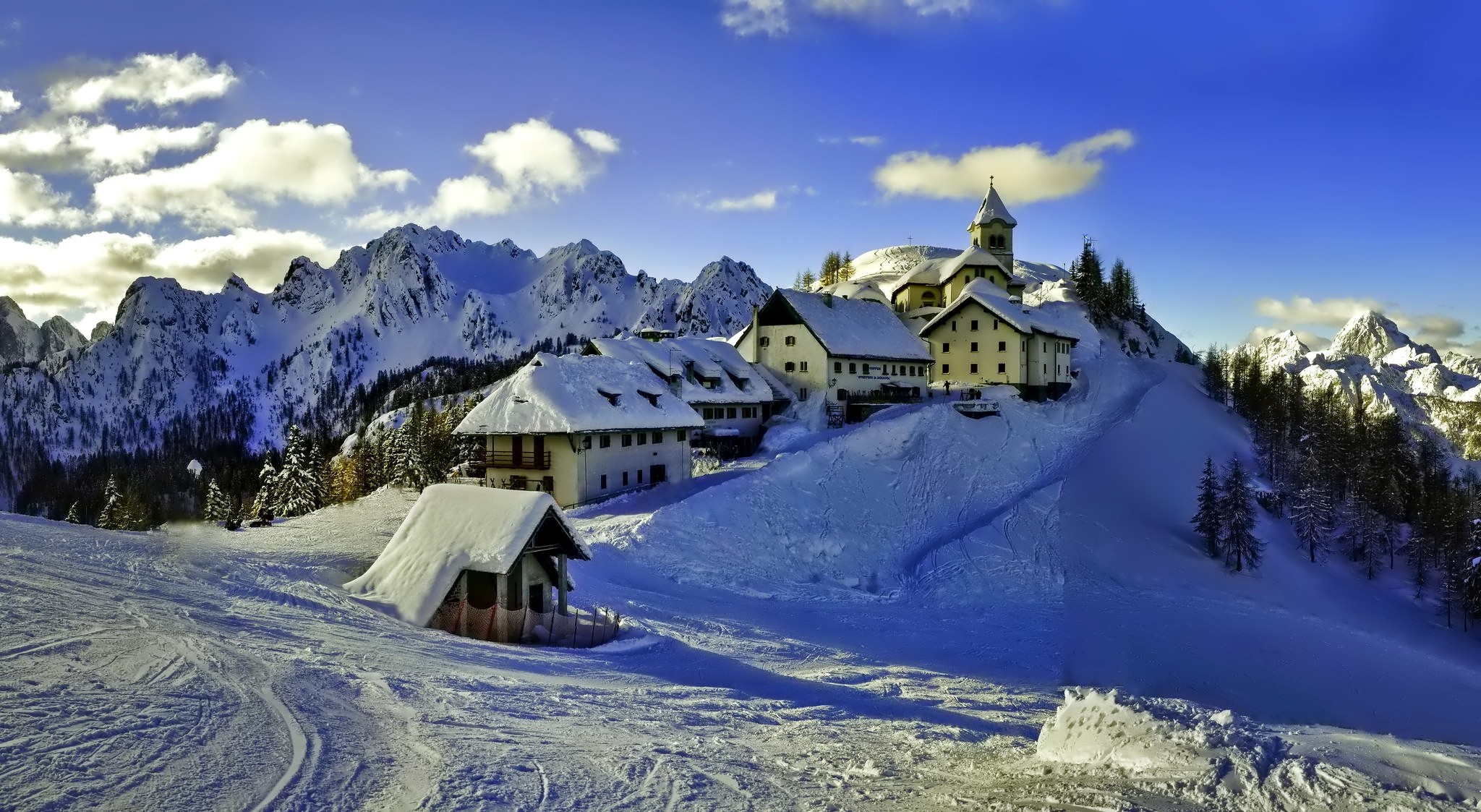 Snowy mountain village with church and ski slopes HD Wallpaper