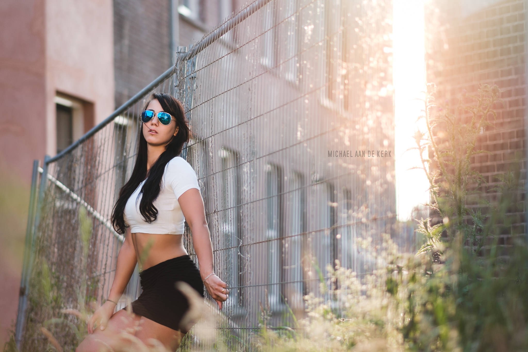 Woman in crop top and shorts posing by fence HD Wallpaper