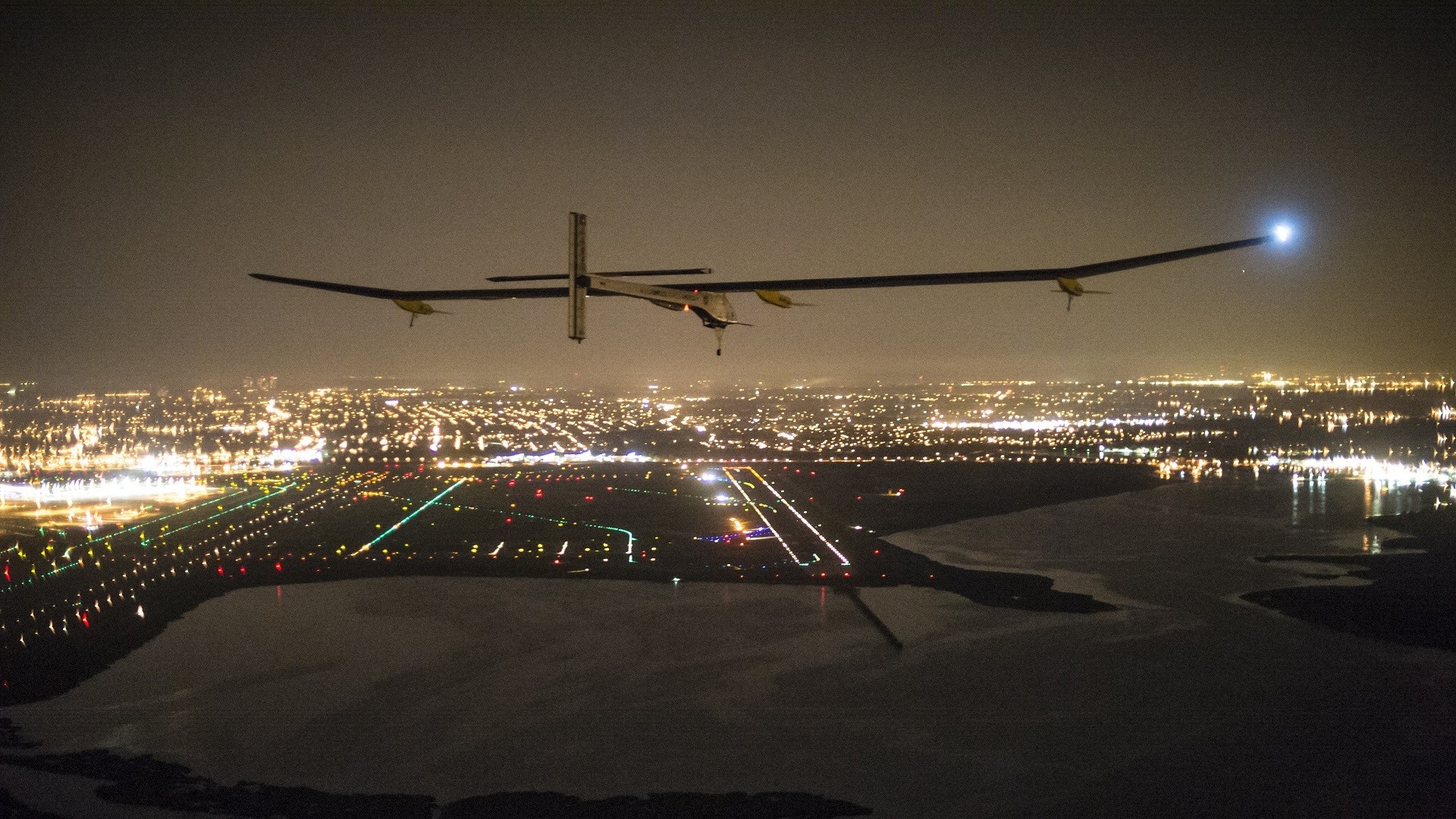 Solar Impulse airplane flying over a city at night HD Wallpaper