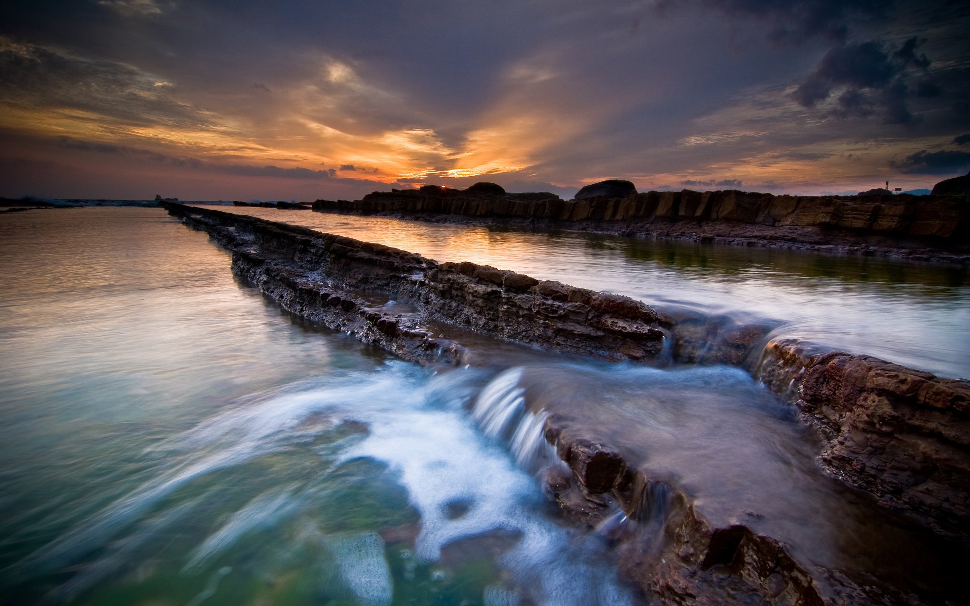 Rocky coastline with water flowing at sunset HD Wallpaper
