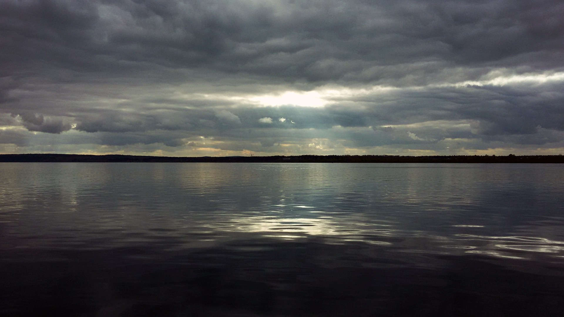 Dark clouds over a calm lake with distant shore HD Wallpaper