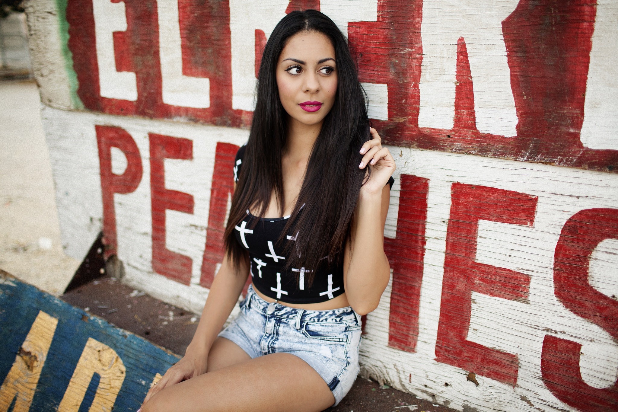 Woman in crop top and jean shorts sitting by a sign HD Wallpaper