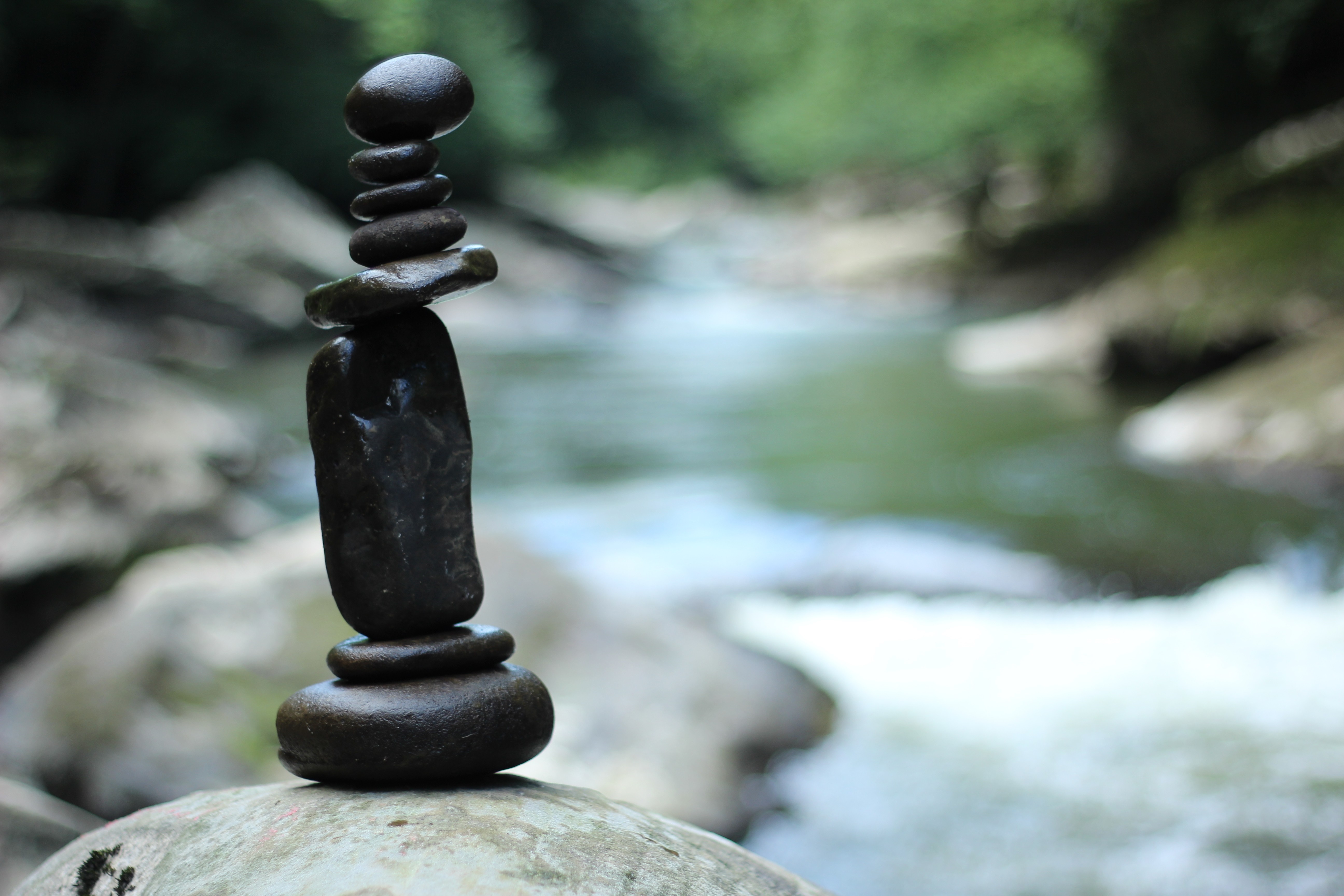 Stacked stones in a river with trees HD Wallpaper