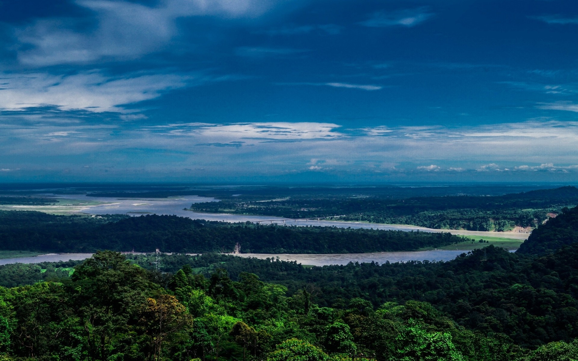 River flowing through lush green landscape under a cloudy sky HD Wallpaper