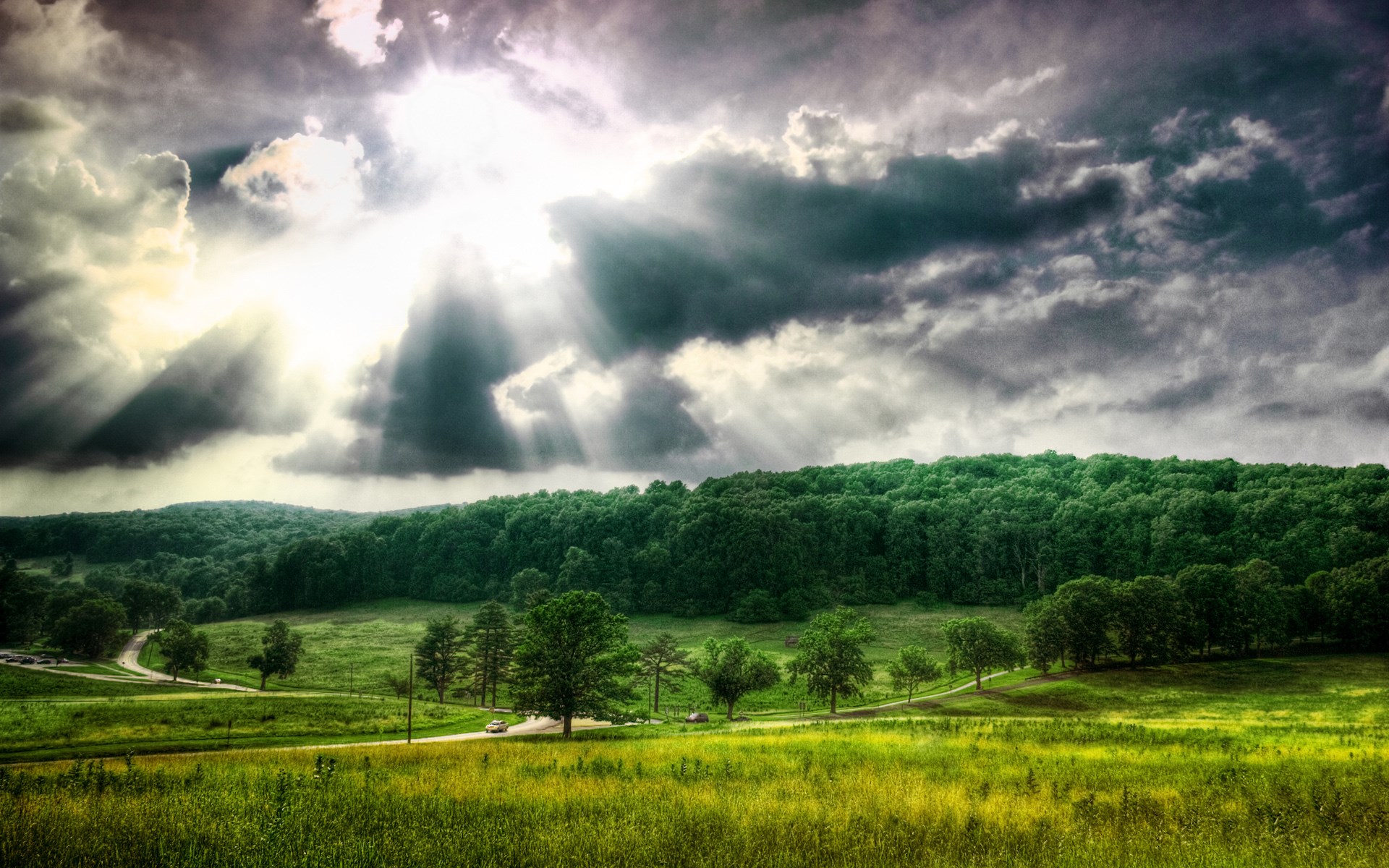Sunbeams through clouds over a green landscape HD Wallpaper