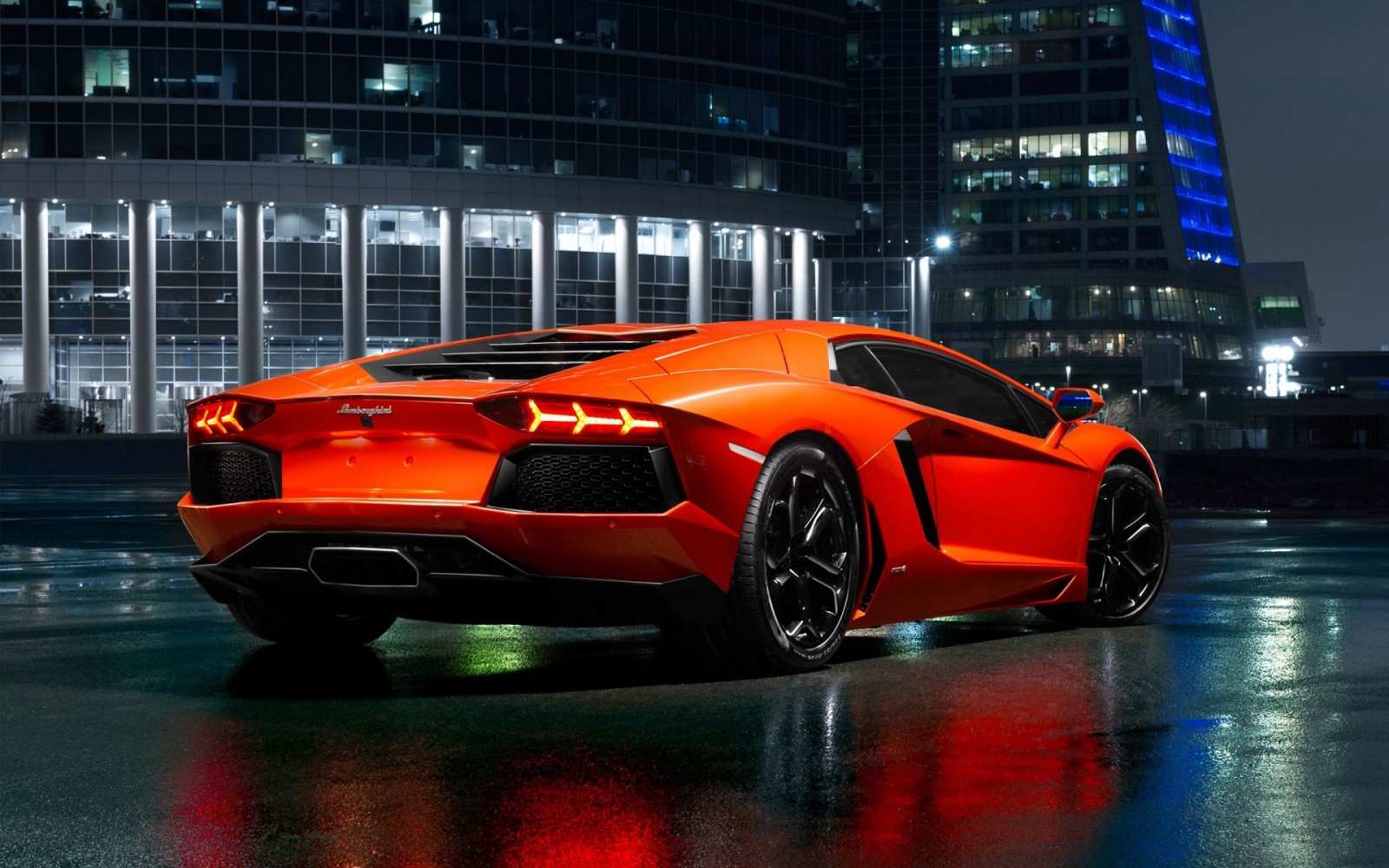 Orange Lamborghini Aventador parked on wet city street at night HD Wallpaper