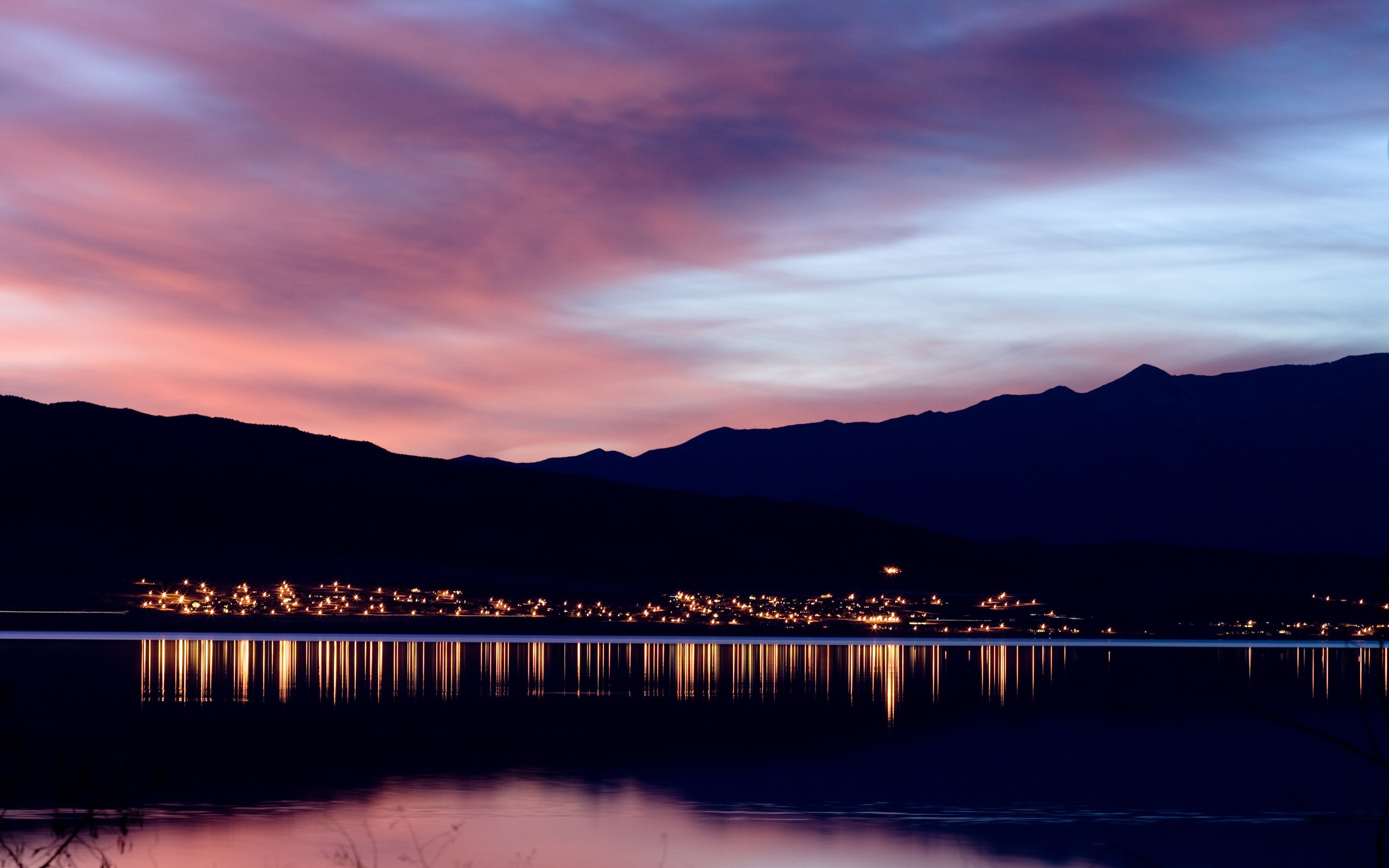 City lights reflected on a lake at sunset with mountains HD Wallpaper