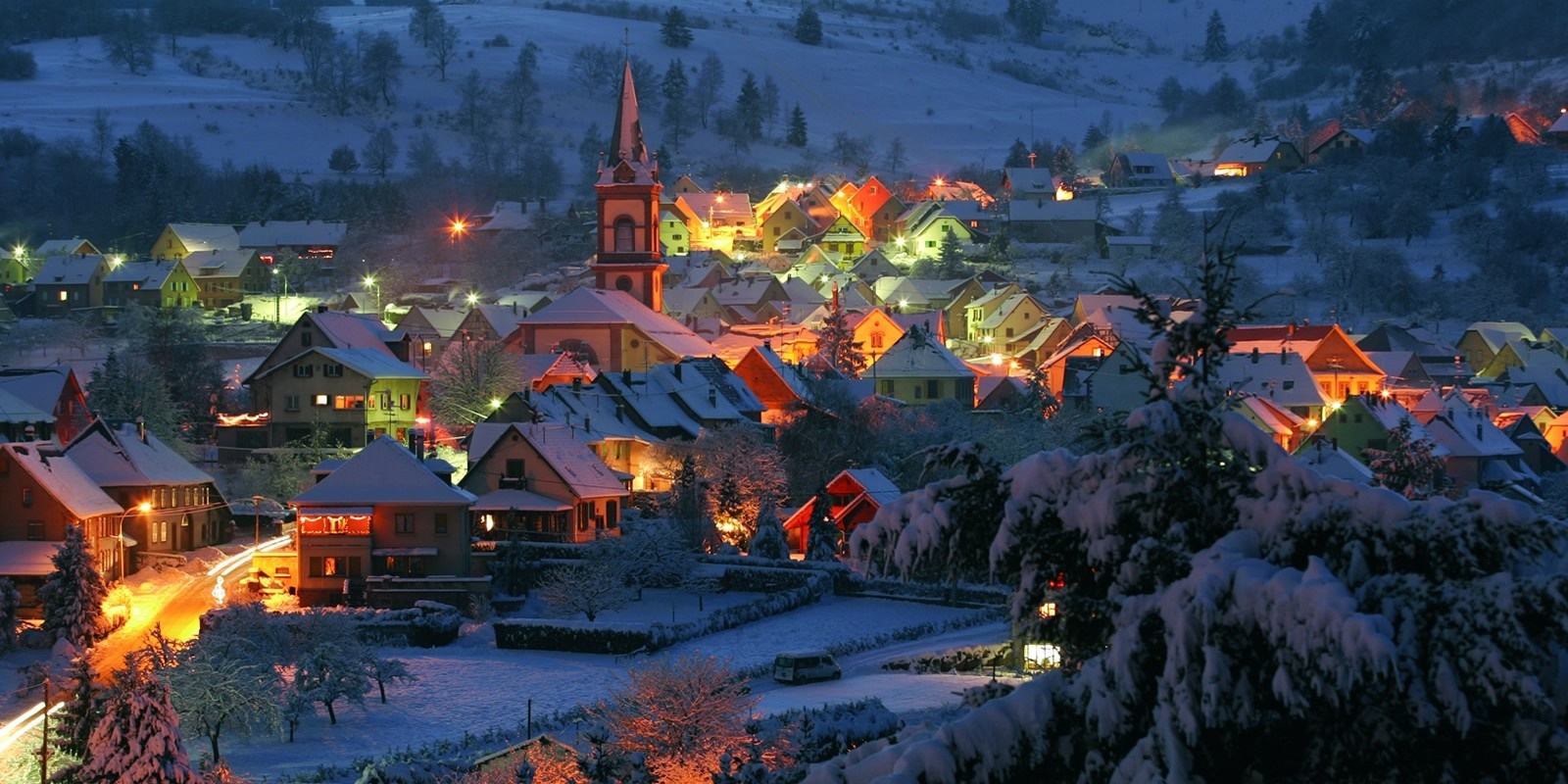 Snowy village at night with illuminated houses and church HD Wallpaper