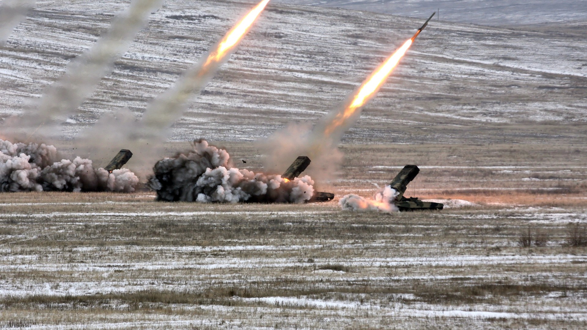 Multiple rockets launching from military vehicles in a field HD Wallpaper