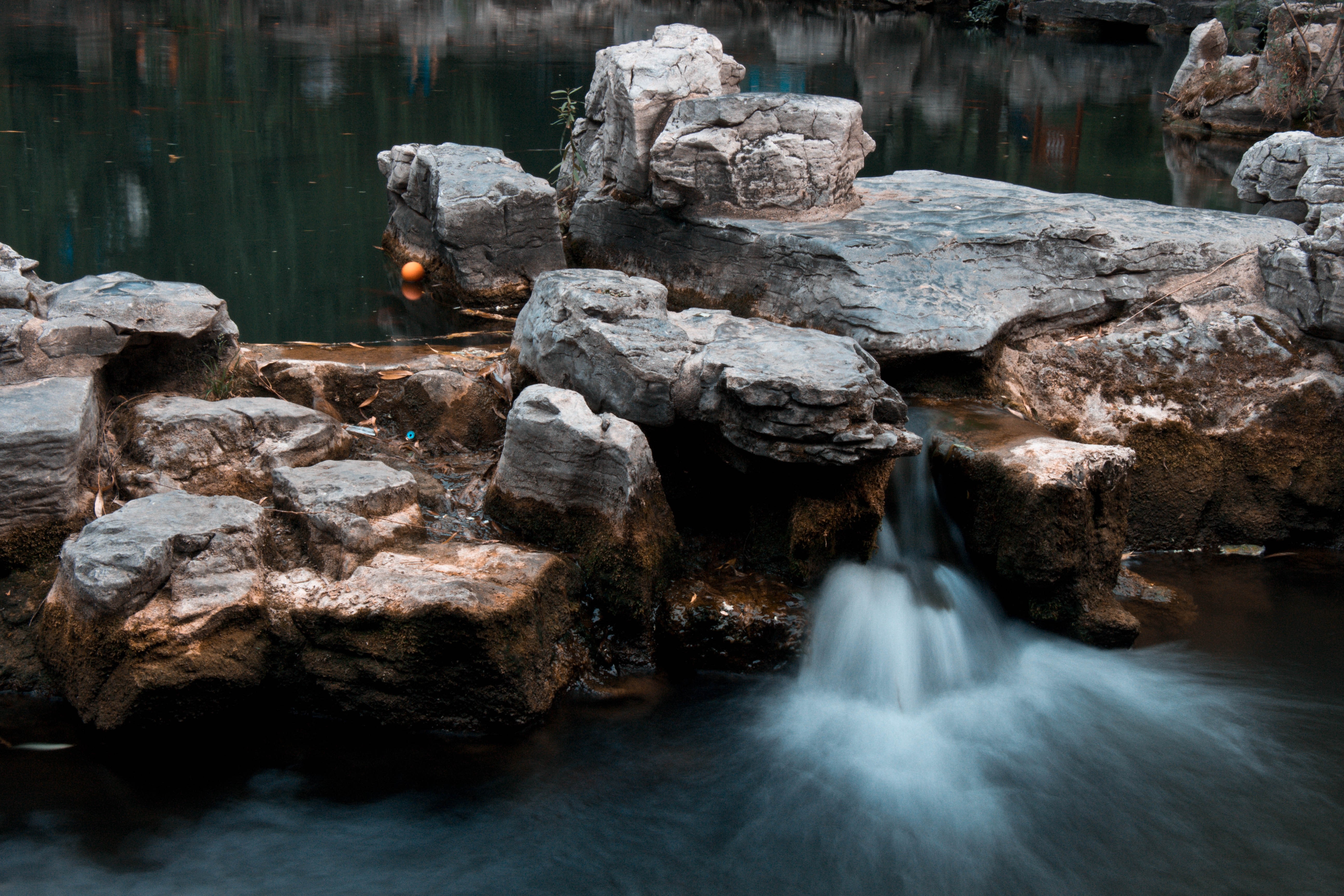 Long exposure of a small waterfall cascading over rocks into a dark body of water HD Wallpaper