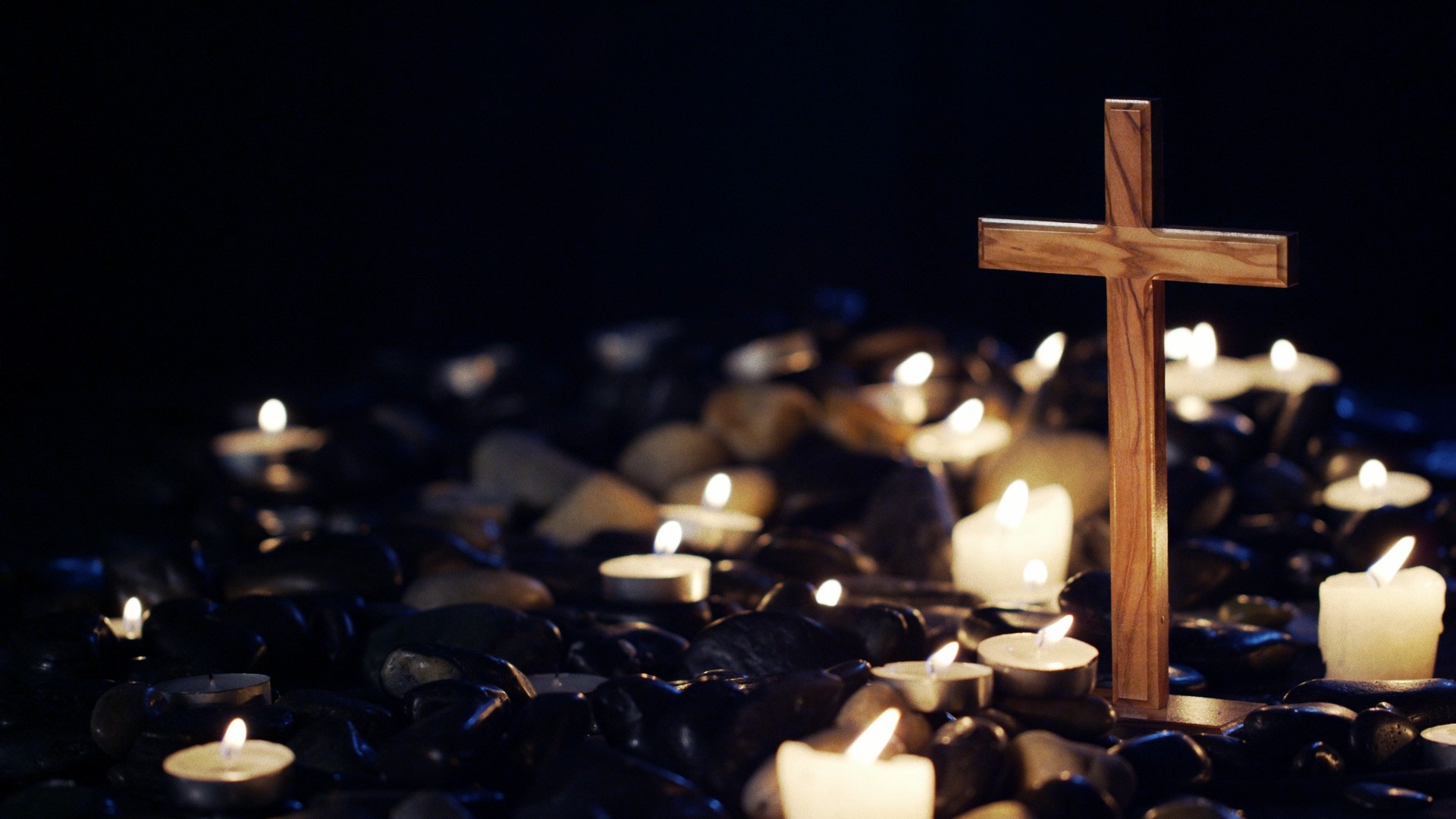 Wooden cross surrounded by lit candles in darkness HD Wallpaper
