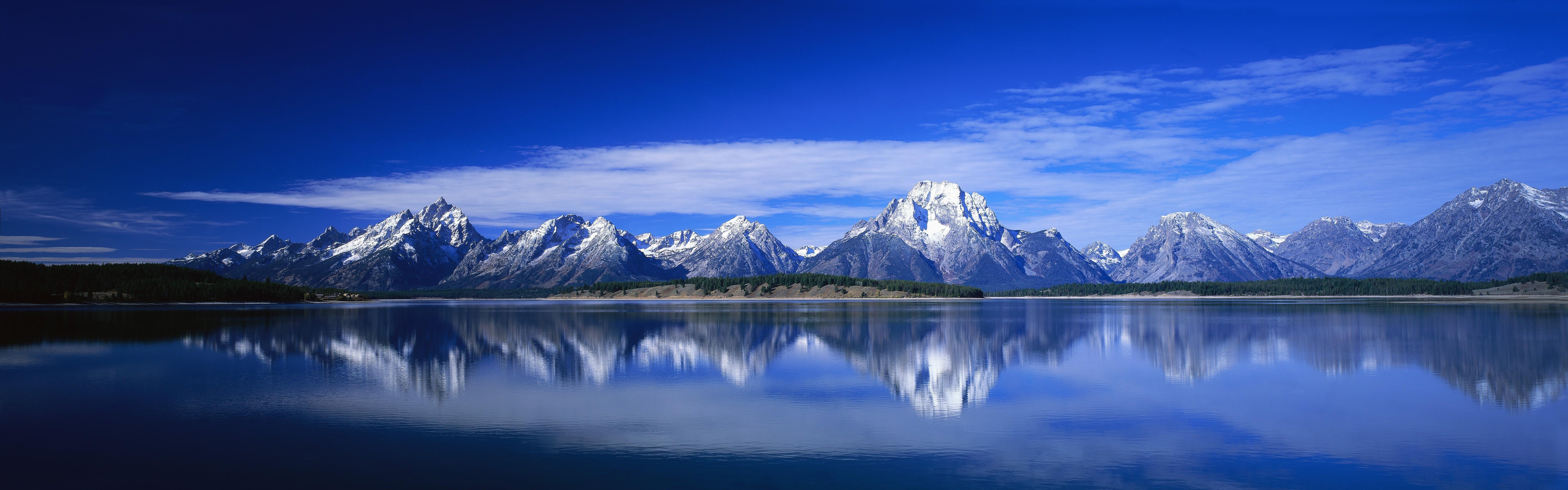 Snow-capped mountains reflected in a calm lake under a blue sky HD Wallpaper