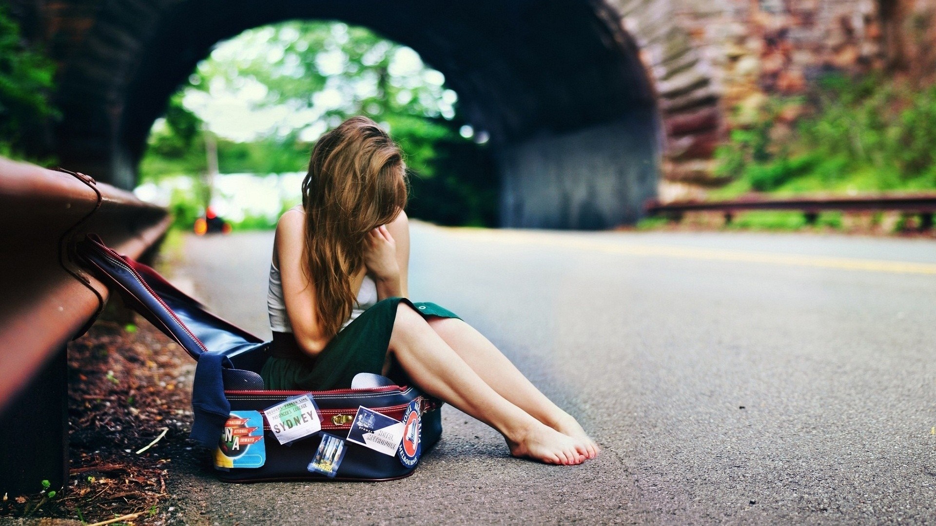 Woman sitting in suitcase by road under tunnel HD Wallpaper