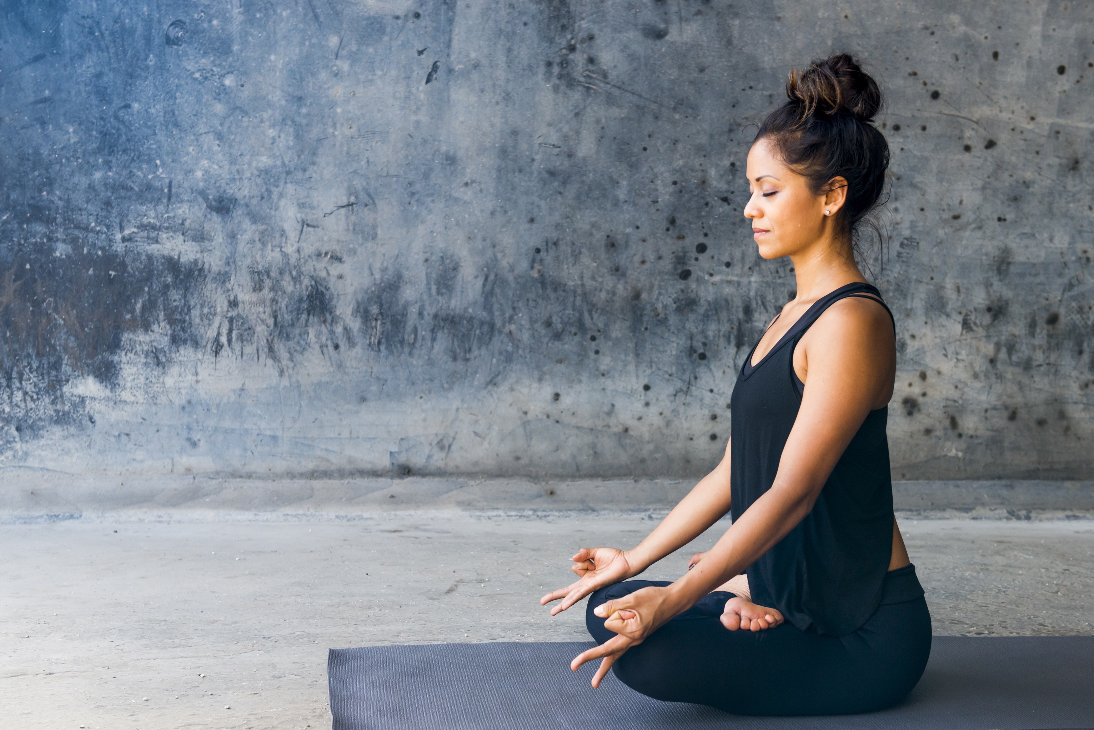 Woman meditating on a yoga mat against a textured wall HD Wallpaper