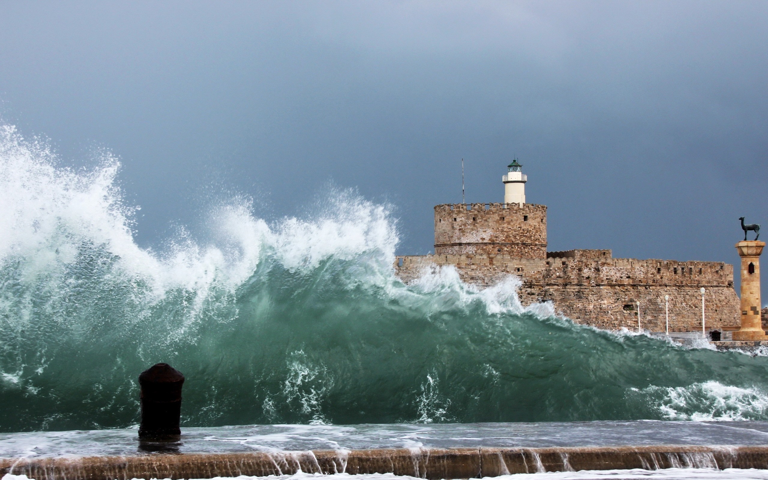 Waves crashing against a stone fort with a lighthouse HD Wallpaper
