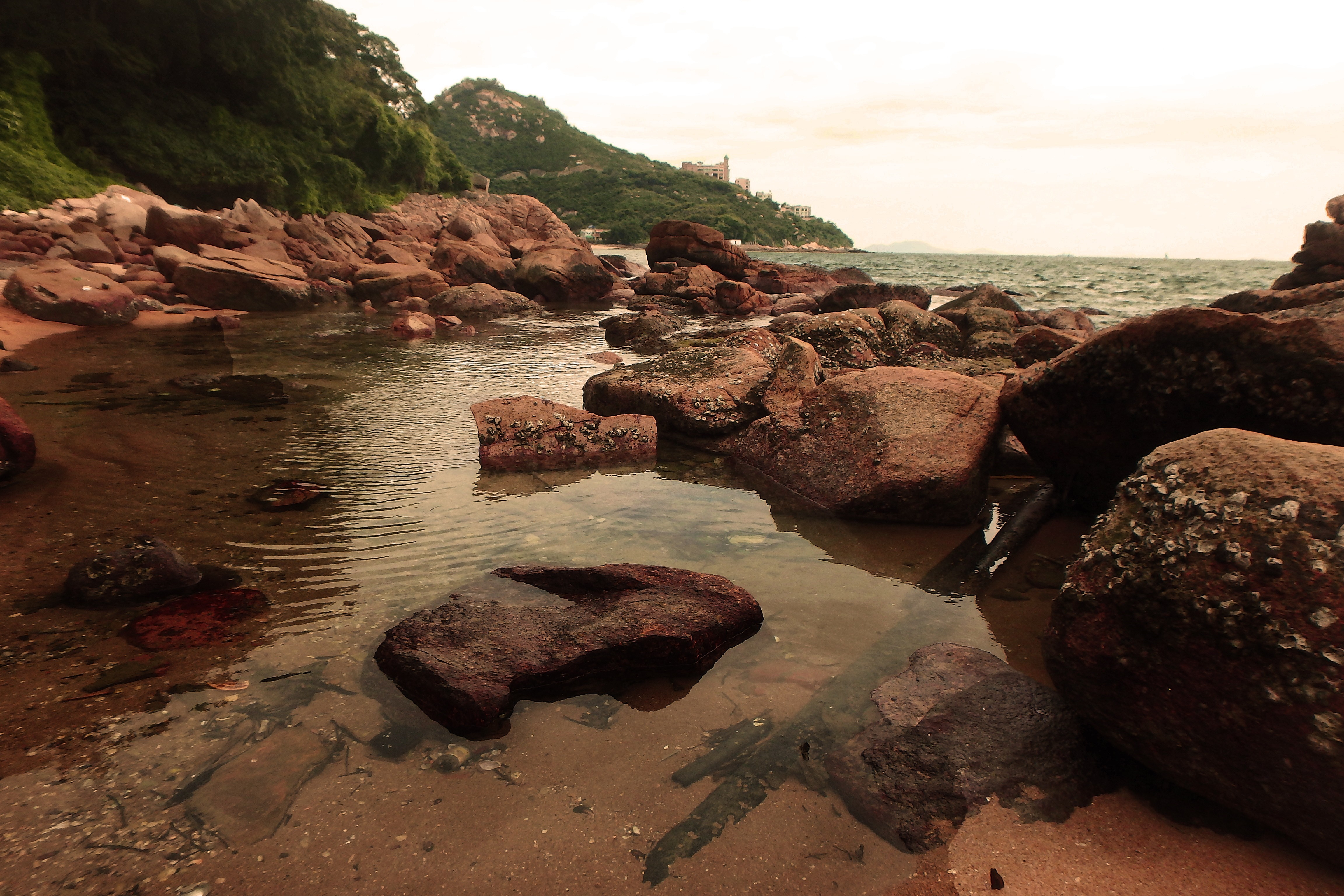 Rocky coastline with calm water and green hills HD Wallpaper