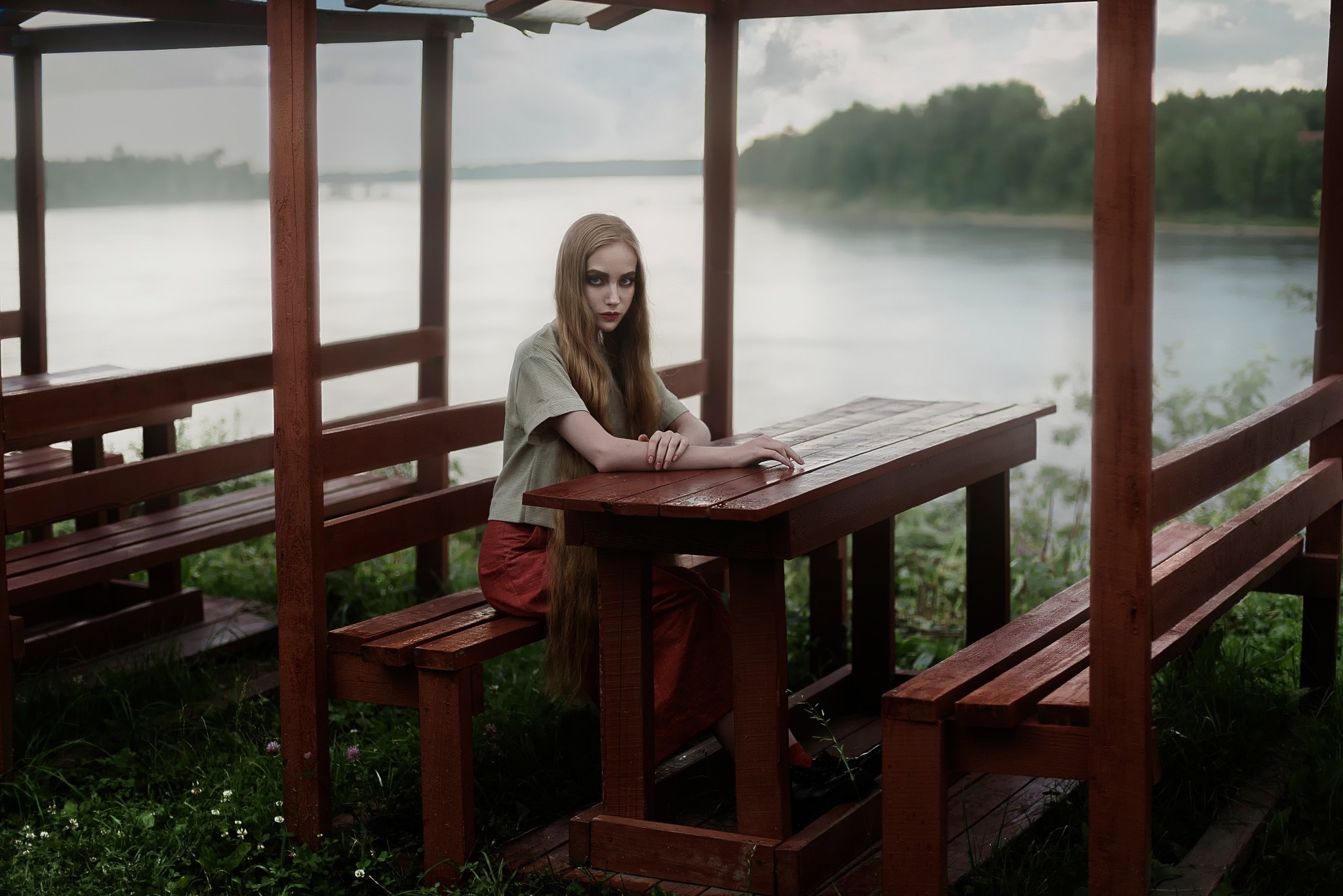 Woman sitting at a wooden table by a lake HD Wallpaper