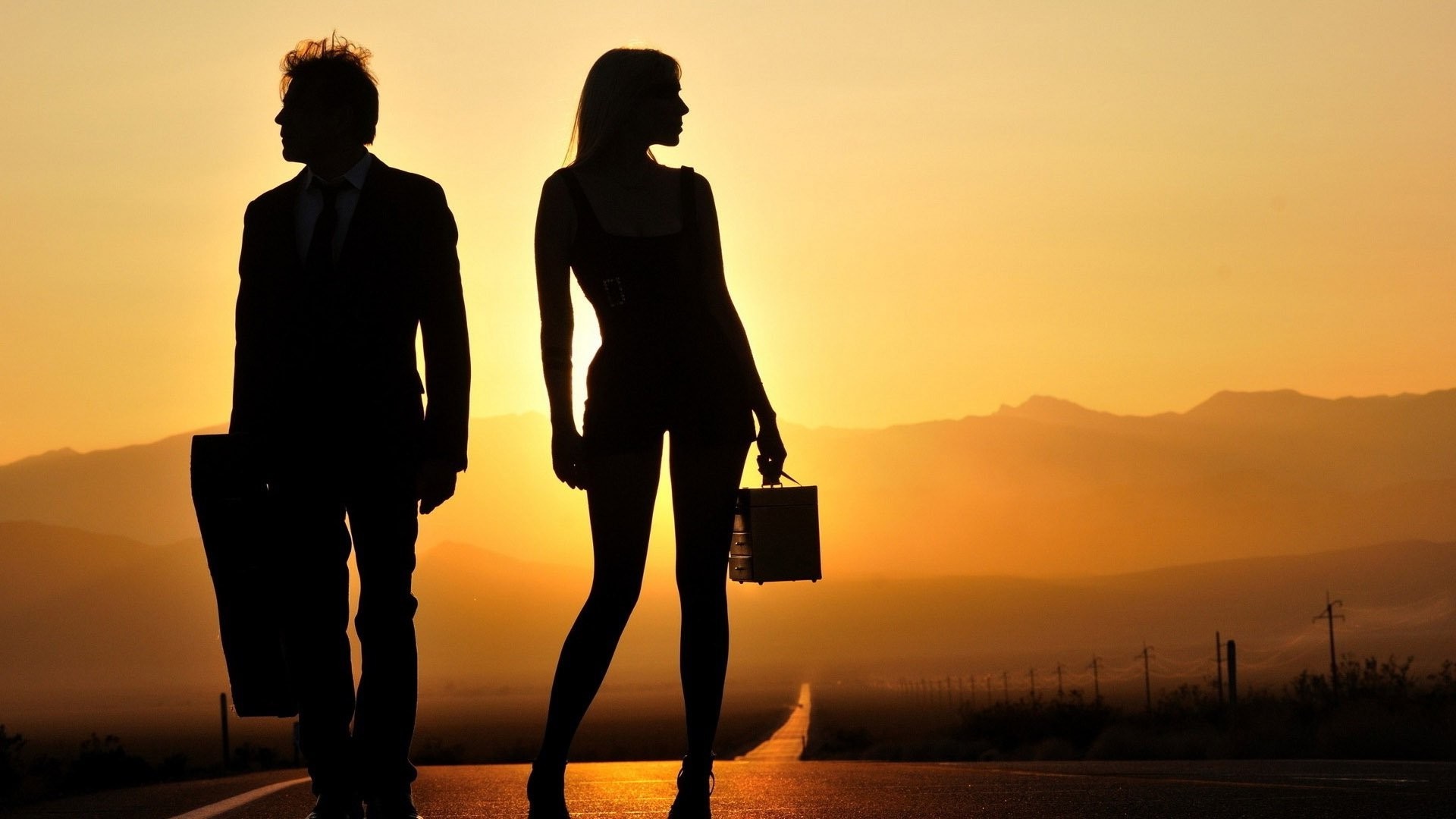 Couple silhouetted on a road at sunset HD Wallpaper