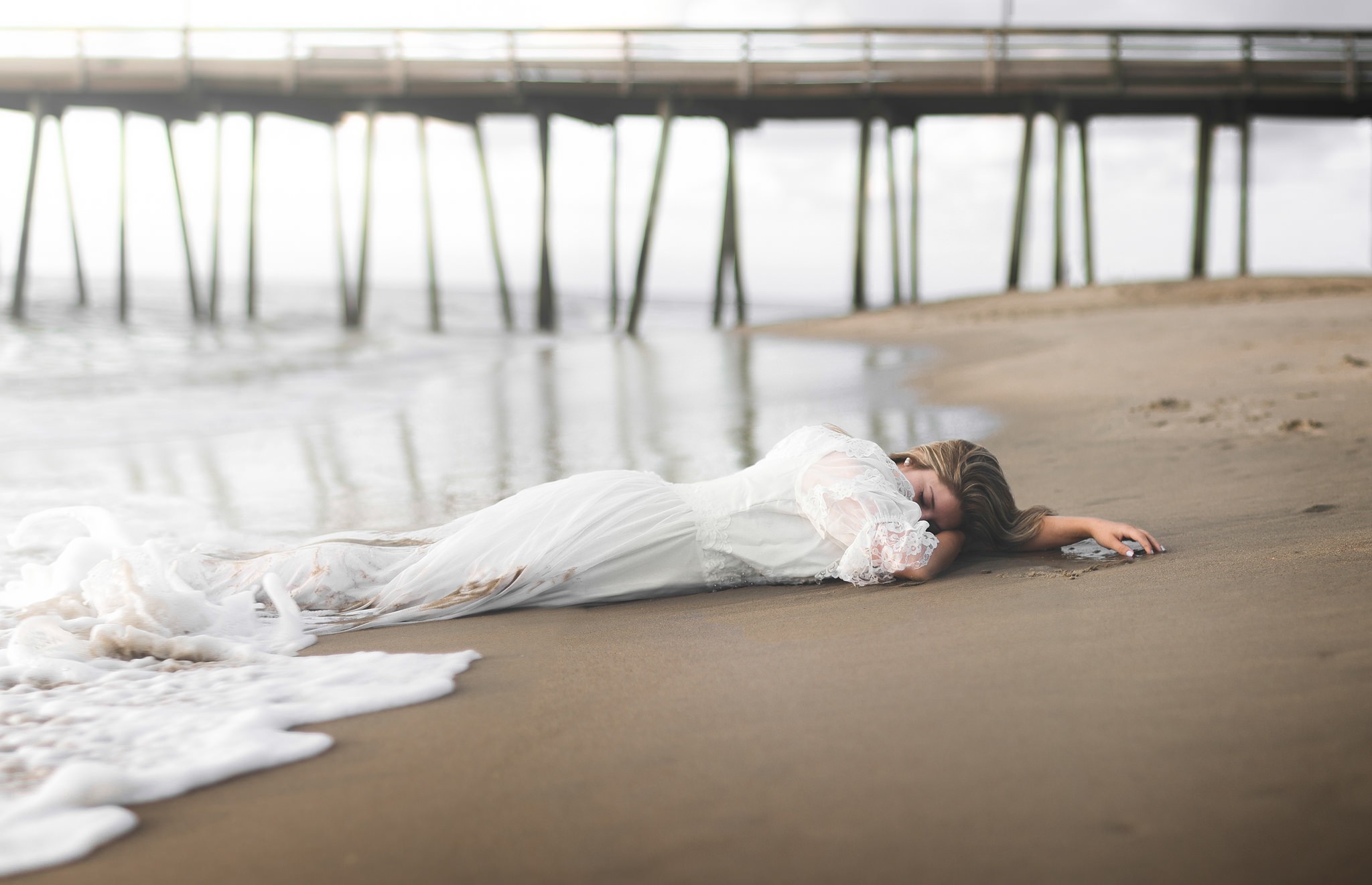 Woman in white dress lying on a beach near a pier HD Wallpaper
