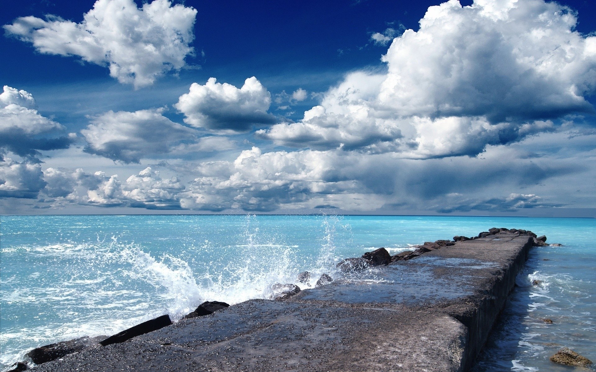 Concrete pier with waves crashing under a cloudy sky HD Wallpaper