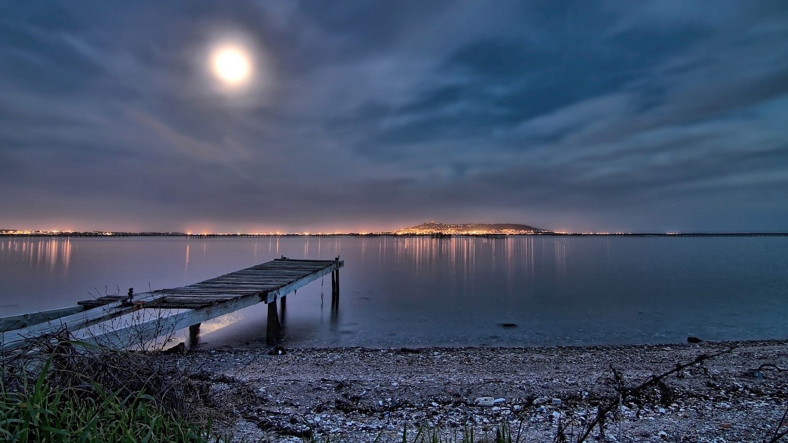 Moonlit dock on a calm lake with distant city lights HD Wallpaper