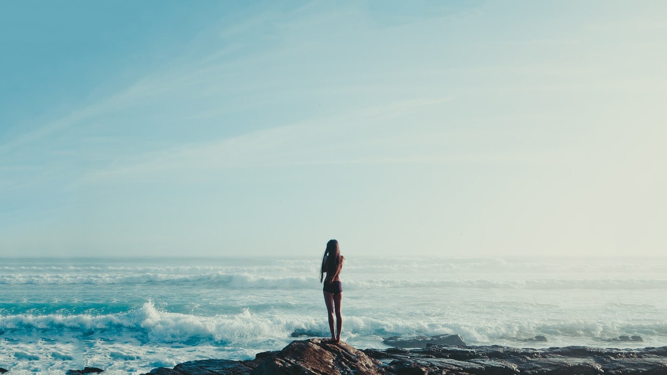 Woman standing on rocks by the ocean with waves HD Wallpaper