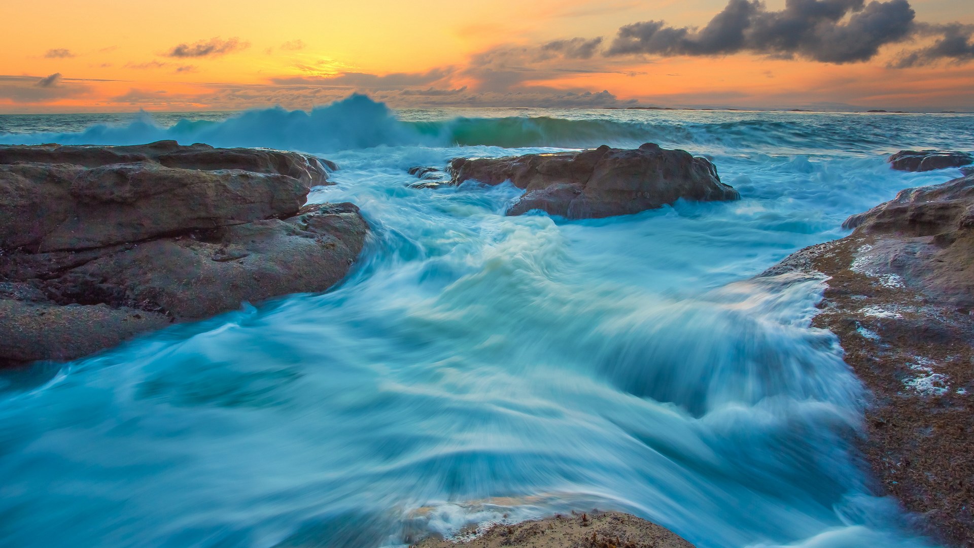 Ocean waves crashing on rocky shore at sunset HD Wallpaper