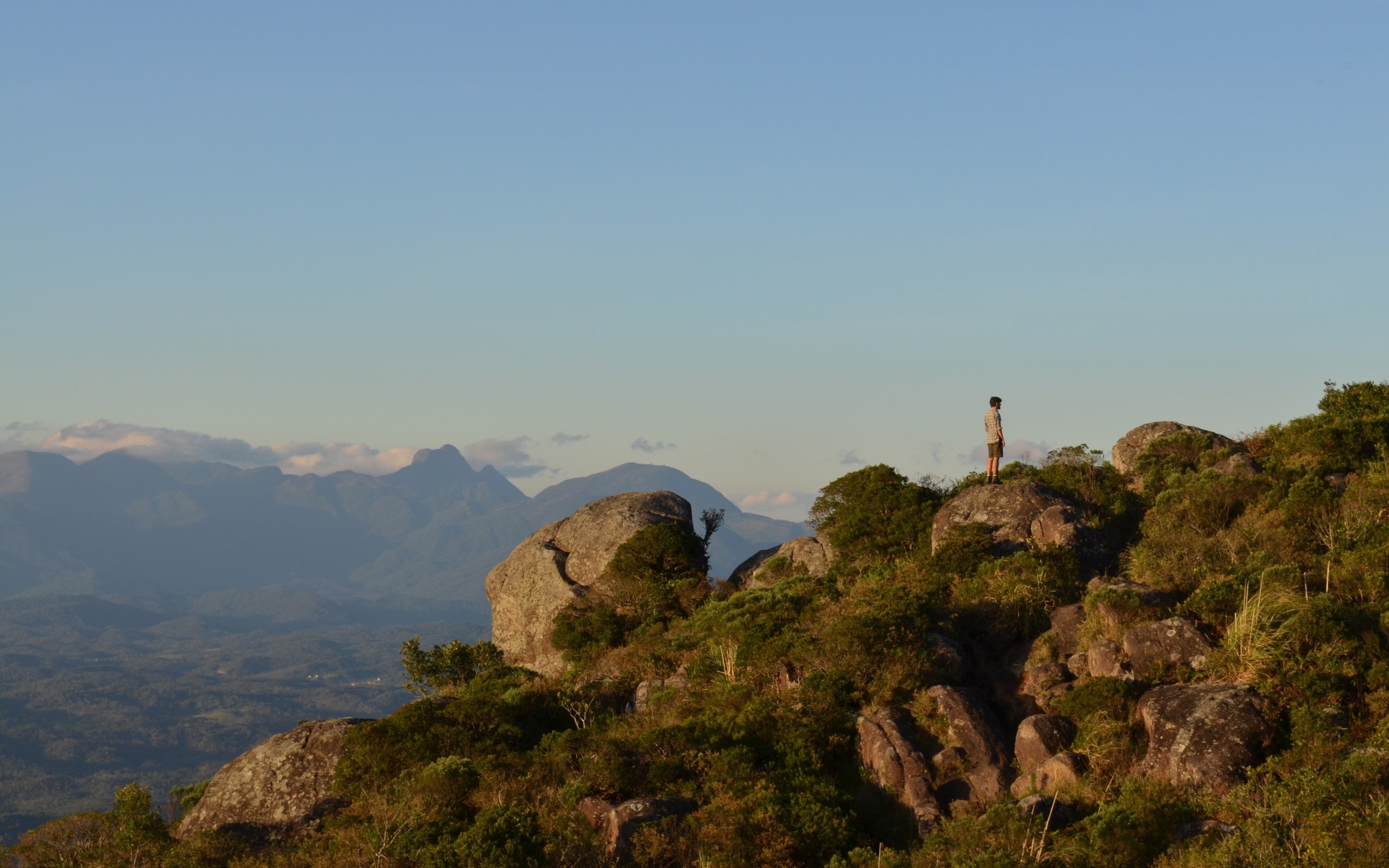 Man standing on a rocky mountain overlooking a valley HD Wallpaper