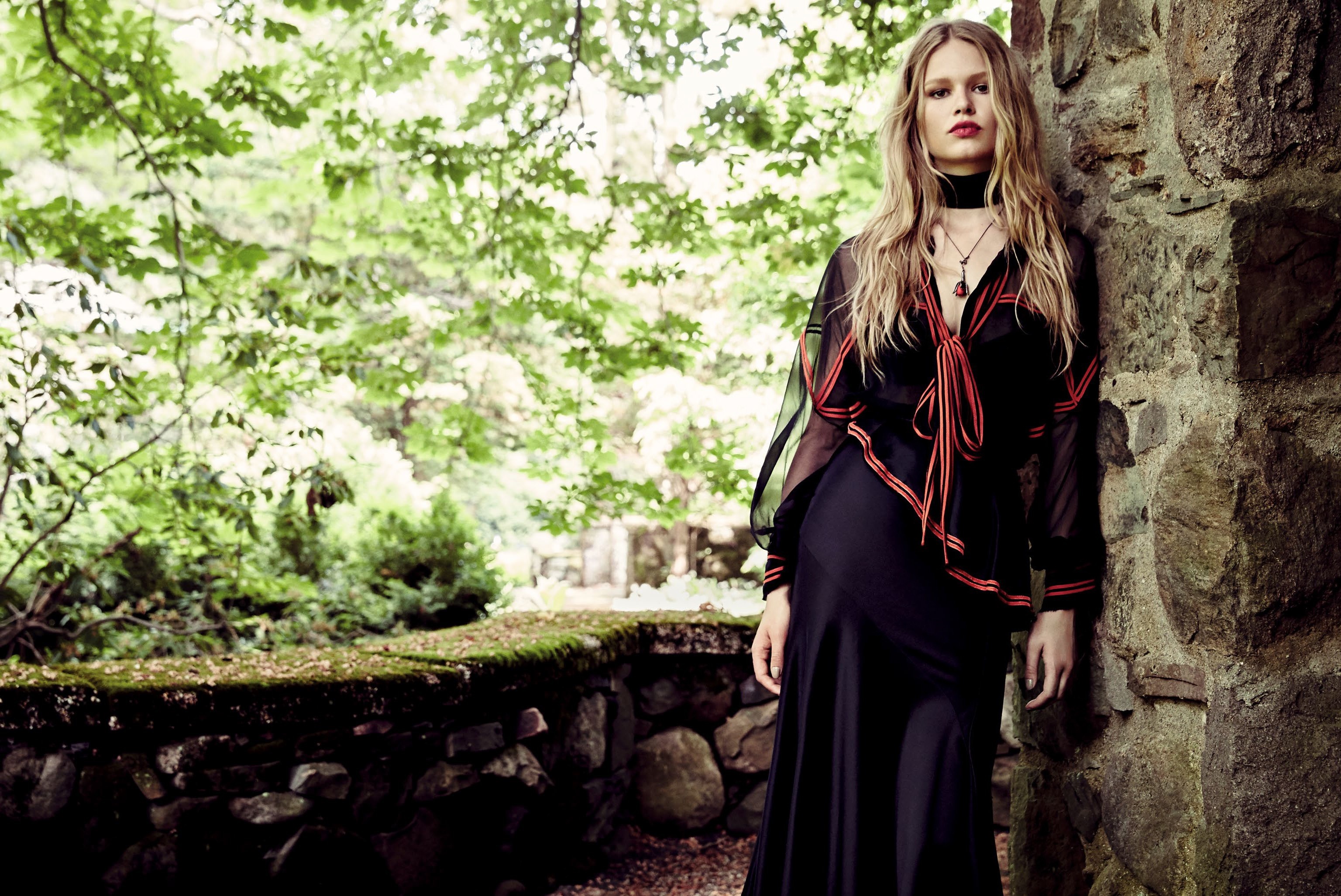 Woman in black dress leaning against stone wall HD Wallpaper