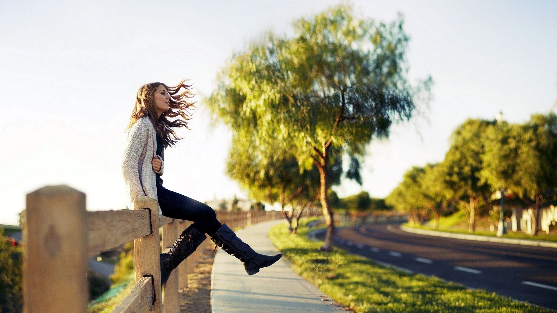 Woman sitting on a fence by a road HD Wallpaper
