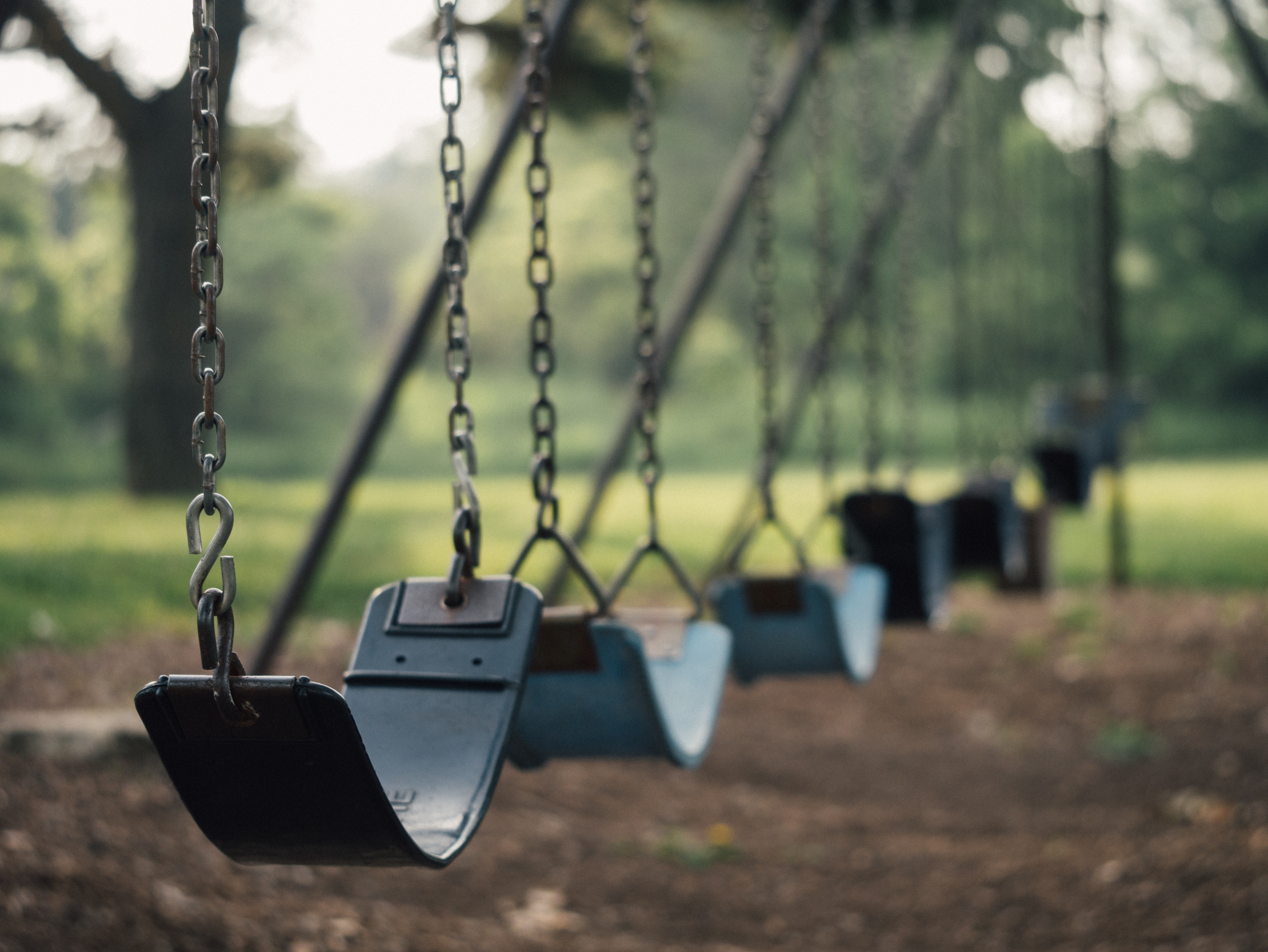Empty swings in a park with trees HD Wallpaper