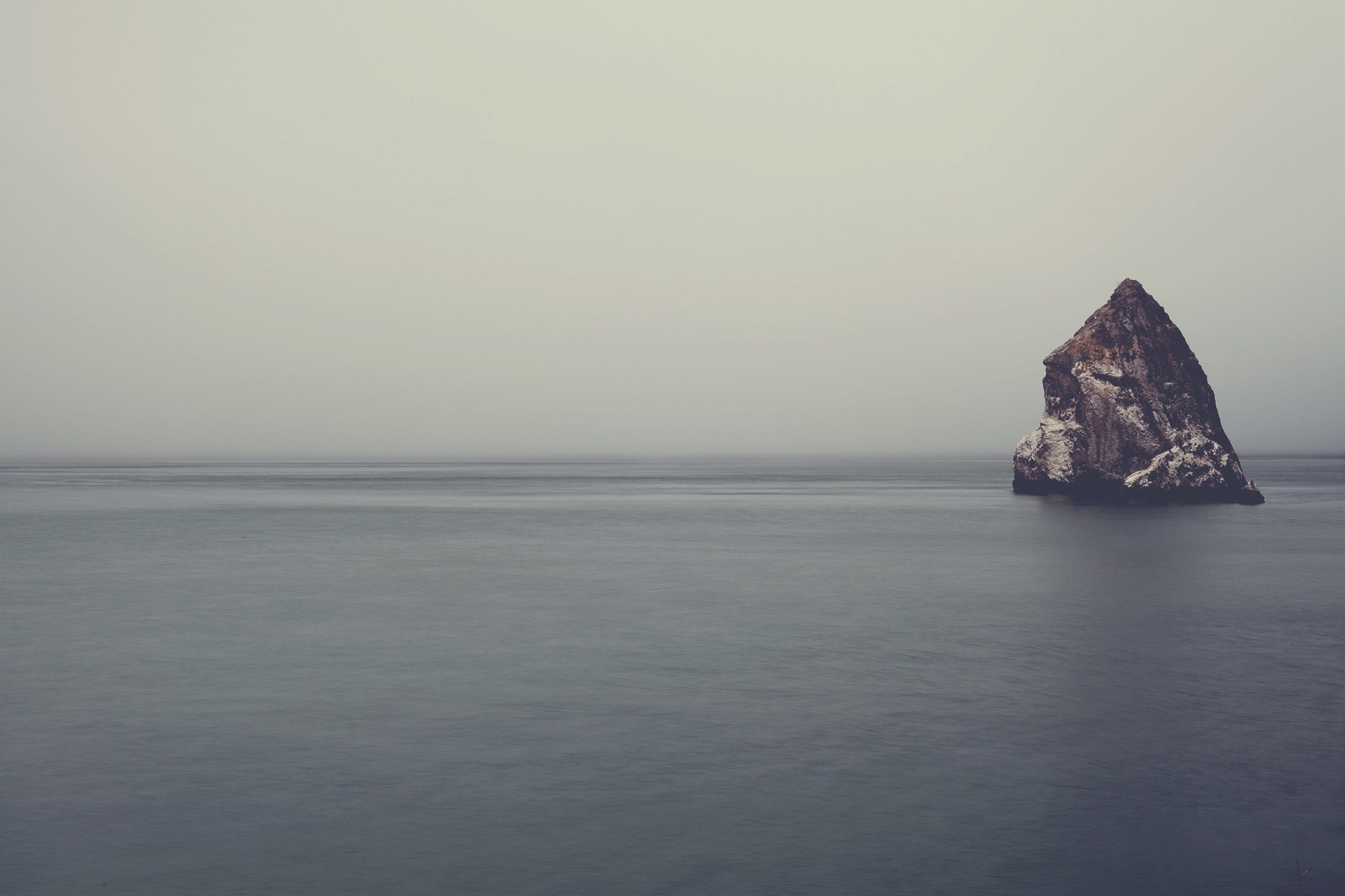 Rock formation in the sea under a foggy sky HD Wallpaper