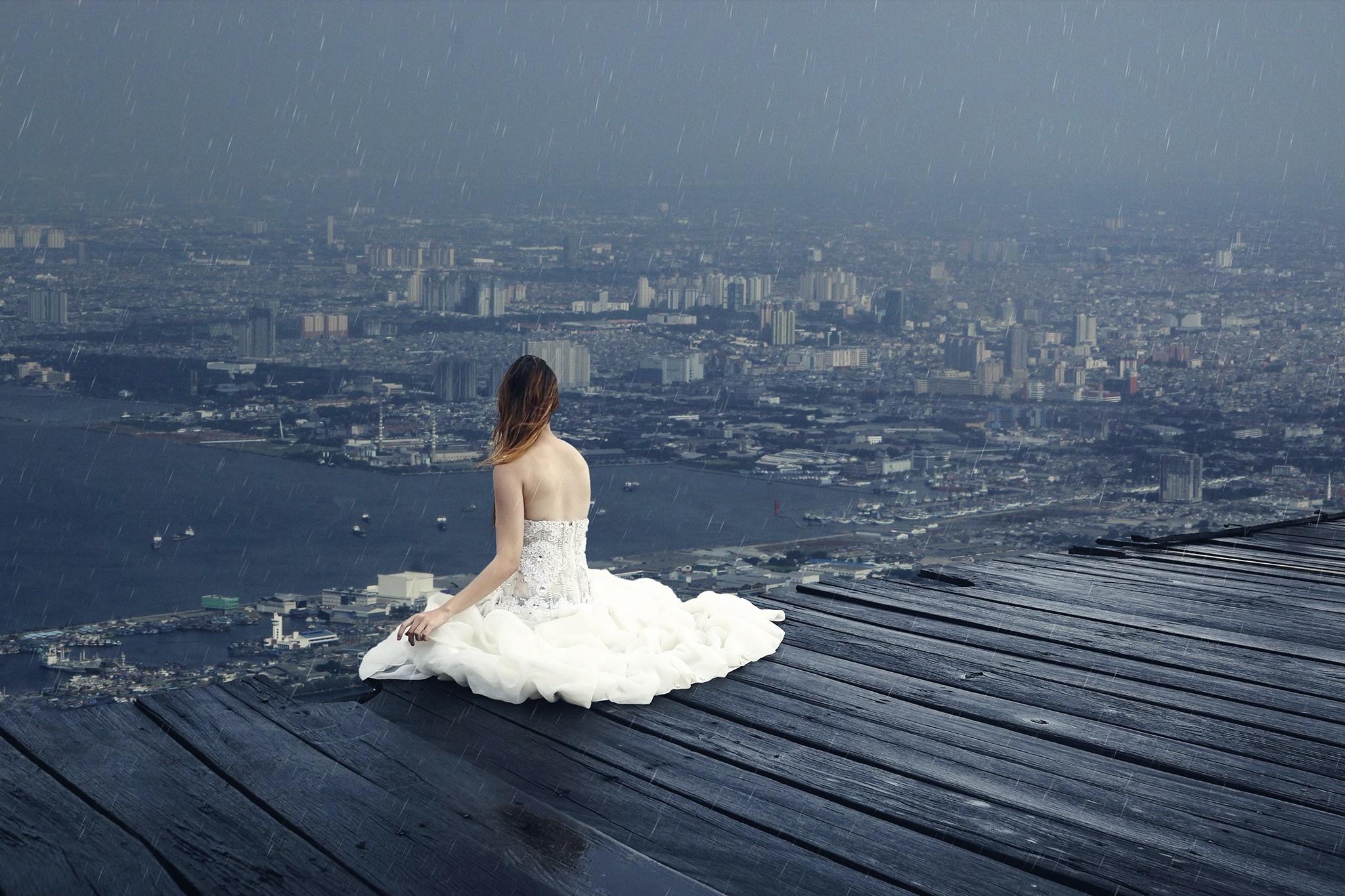 Woman in white dress sitting on wooden planks overlooking city in rain HD Wallpaper