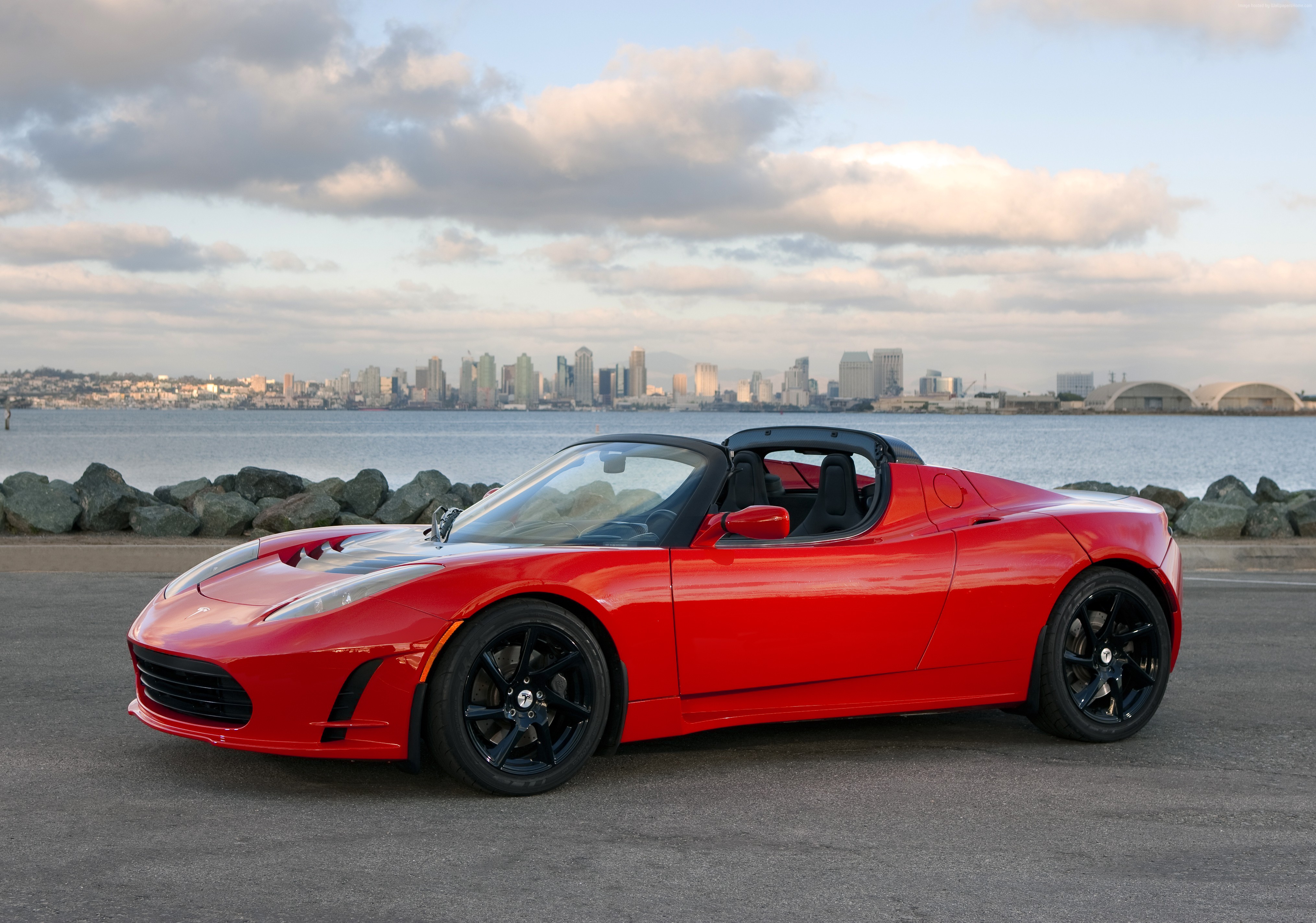 Red Tesla Roadster Sport parked by the water with city skyline HD Wallpaper