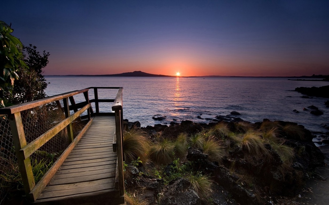 Wooden walkway overlooking the sea at sunset with an island on the horizon HD Wallpaper