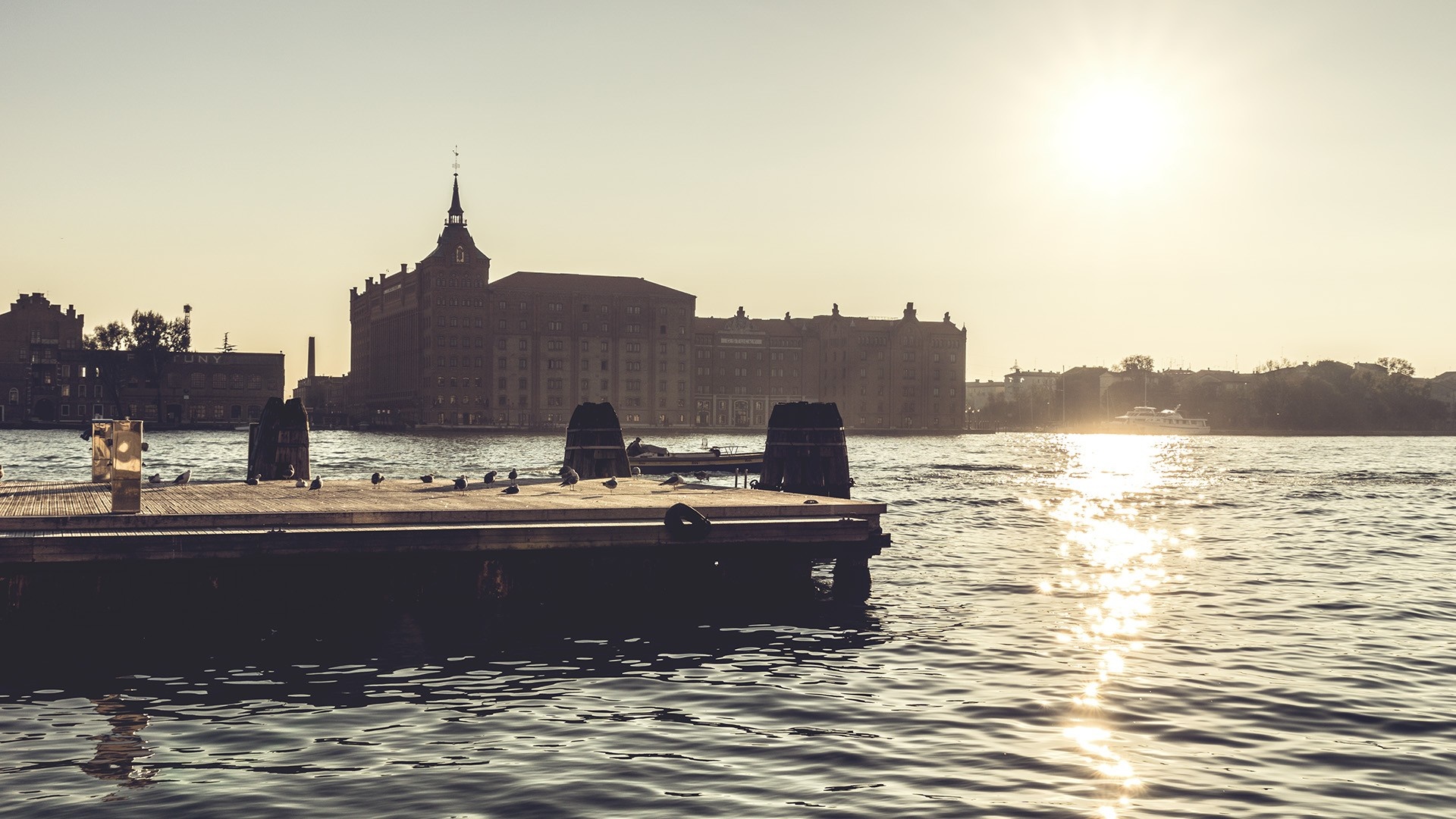 Sunset over a city skyline with a pier and boat HD Wallpaper