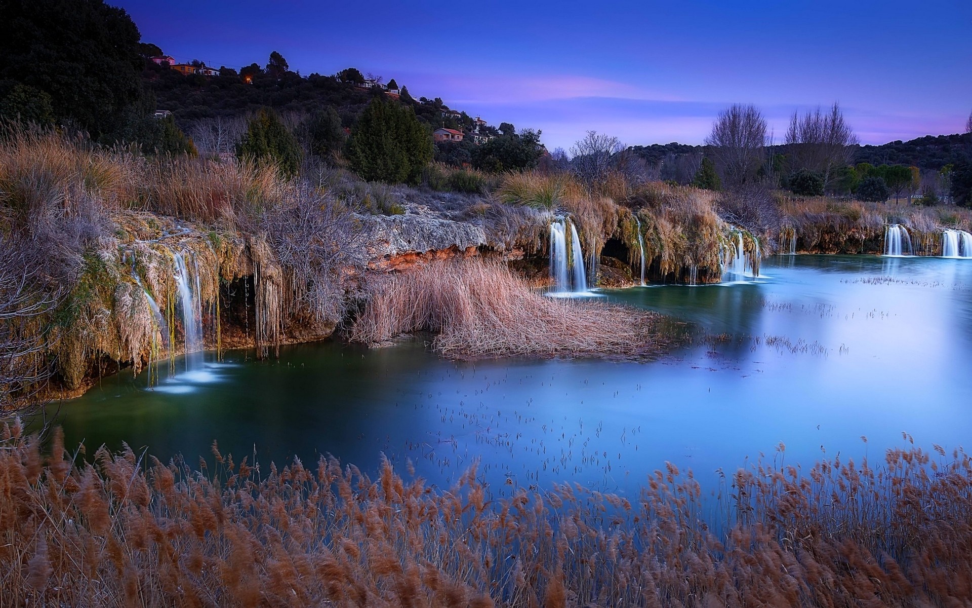 Waterfalls cascade into a tranquil lake at dusk HD Wallpaper