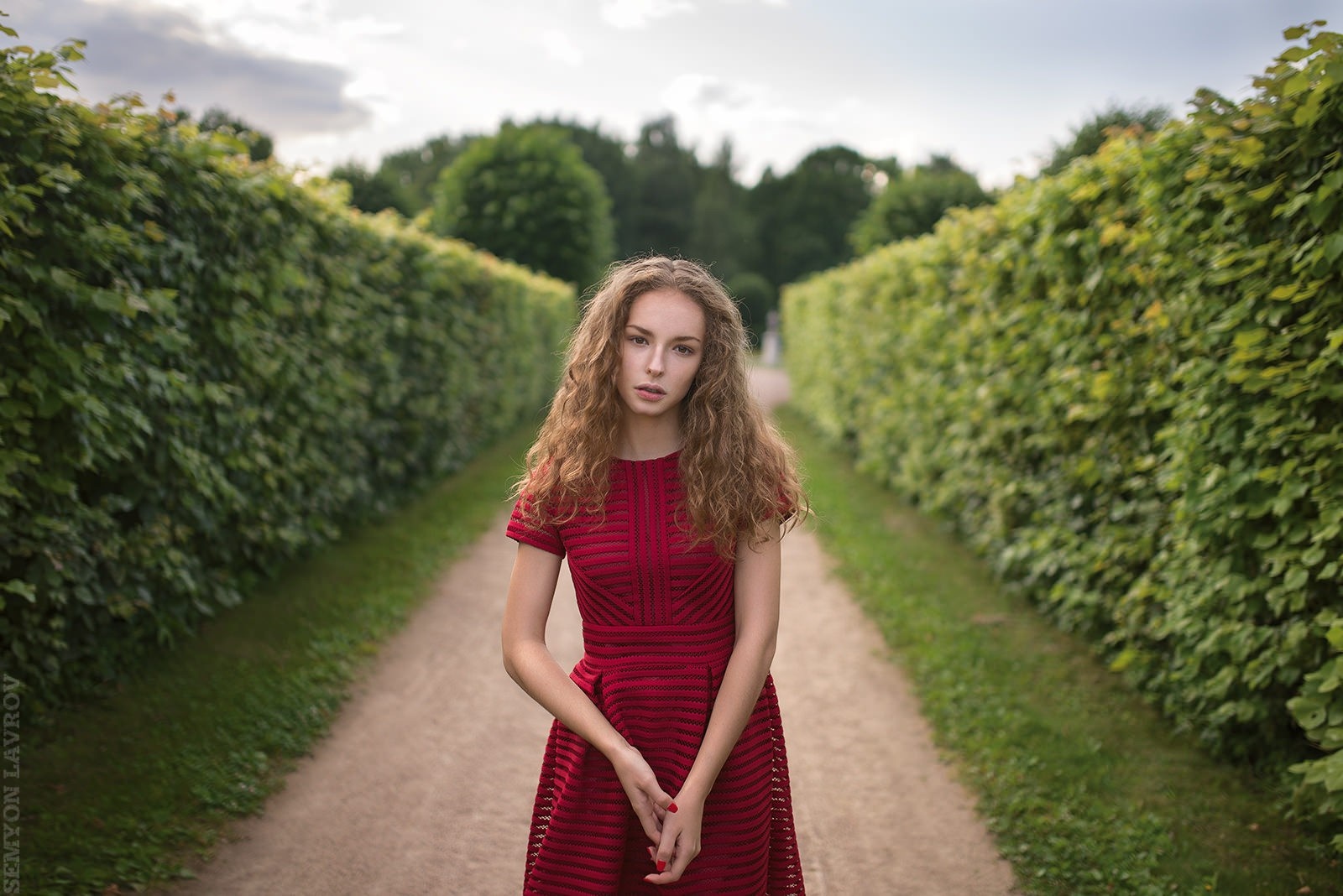 Woman in red dress standing on path between hedges HD Wallpaper
