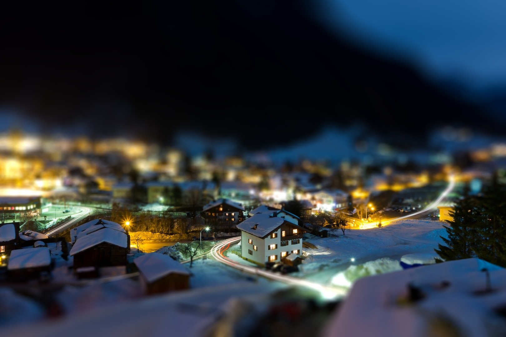 Tilt-shift night view of a snowy village with light trails HD Wallpaper