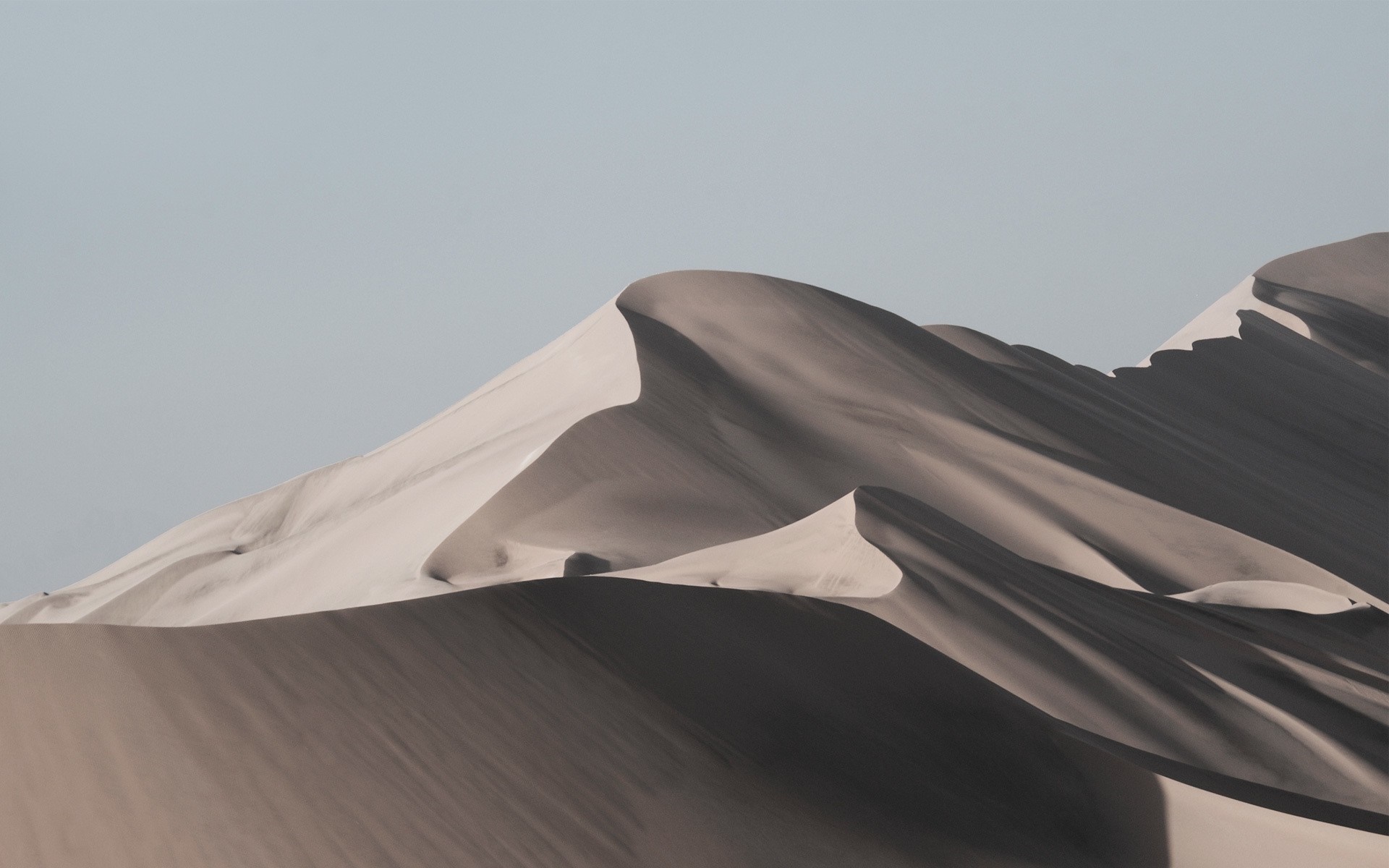 Sand dunes shaped by wind under a clear sky HD Wallpaper