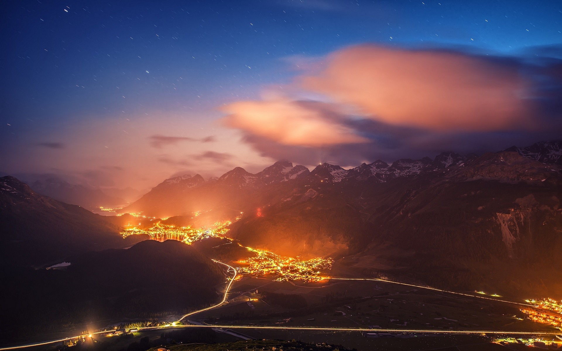 Mountain village lights at night with stars and clouds HD Wallpaper