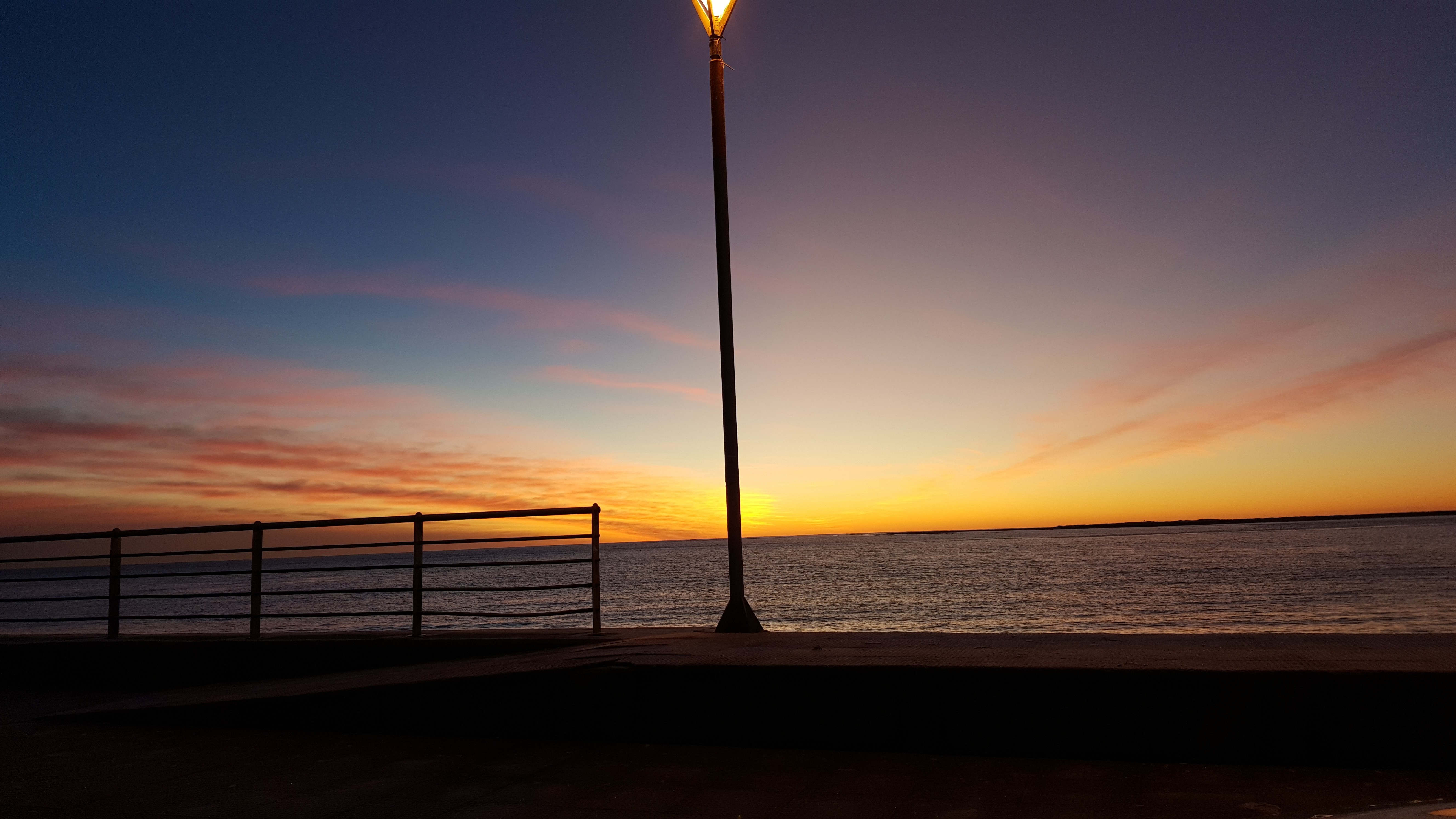 Sunset over the sea with a lamppost and railing HD Wallpaper