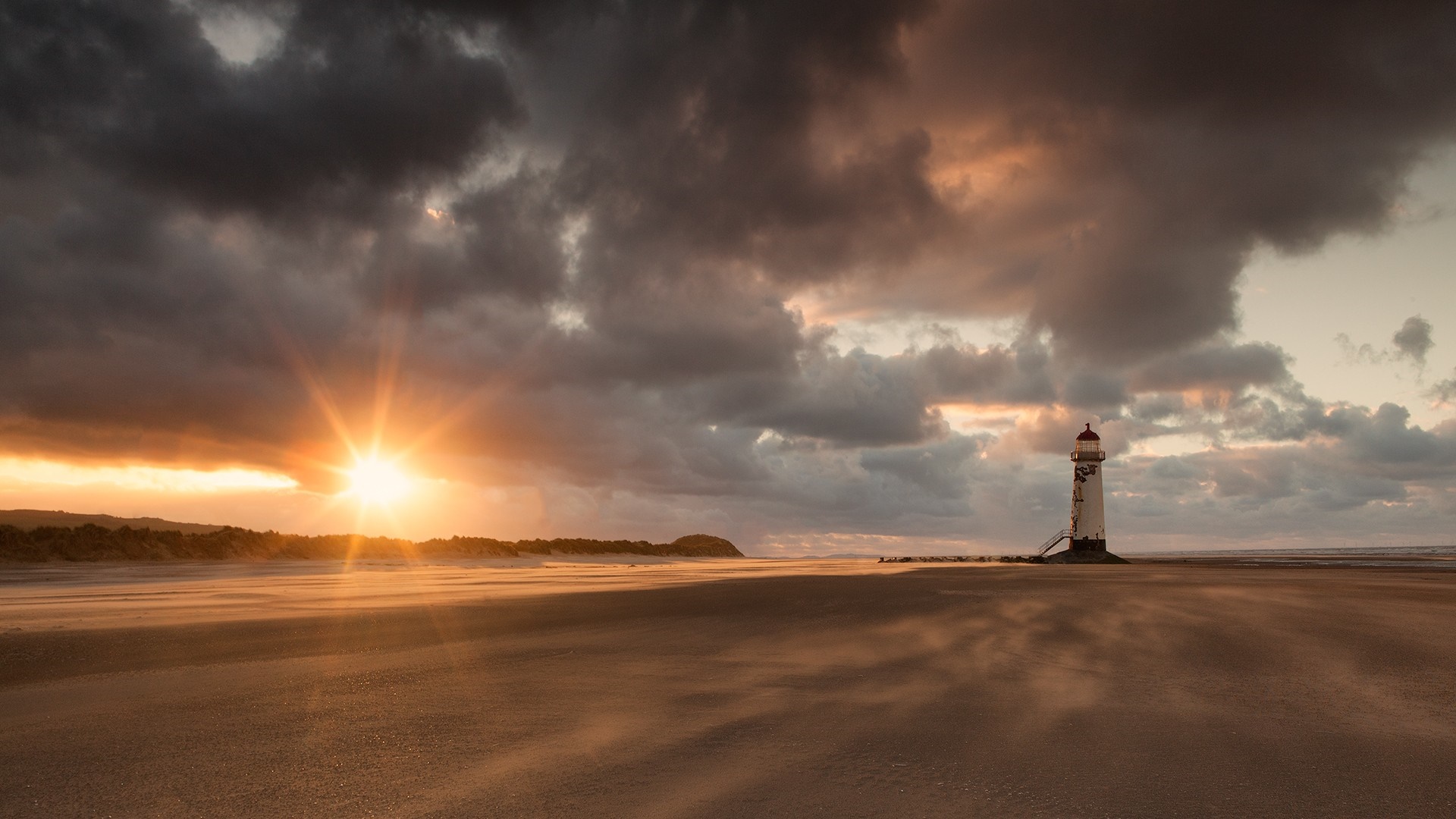 Lighthouse on a sandy beach at sunset with dramatic clouds HD Wallpaper